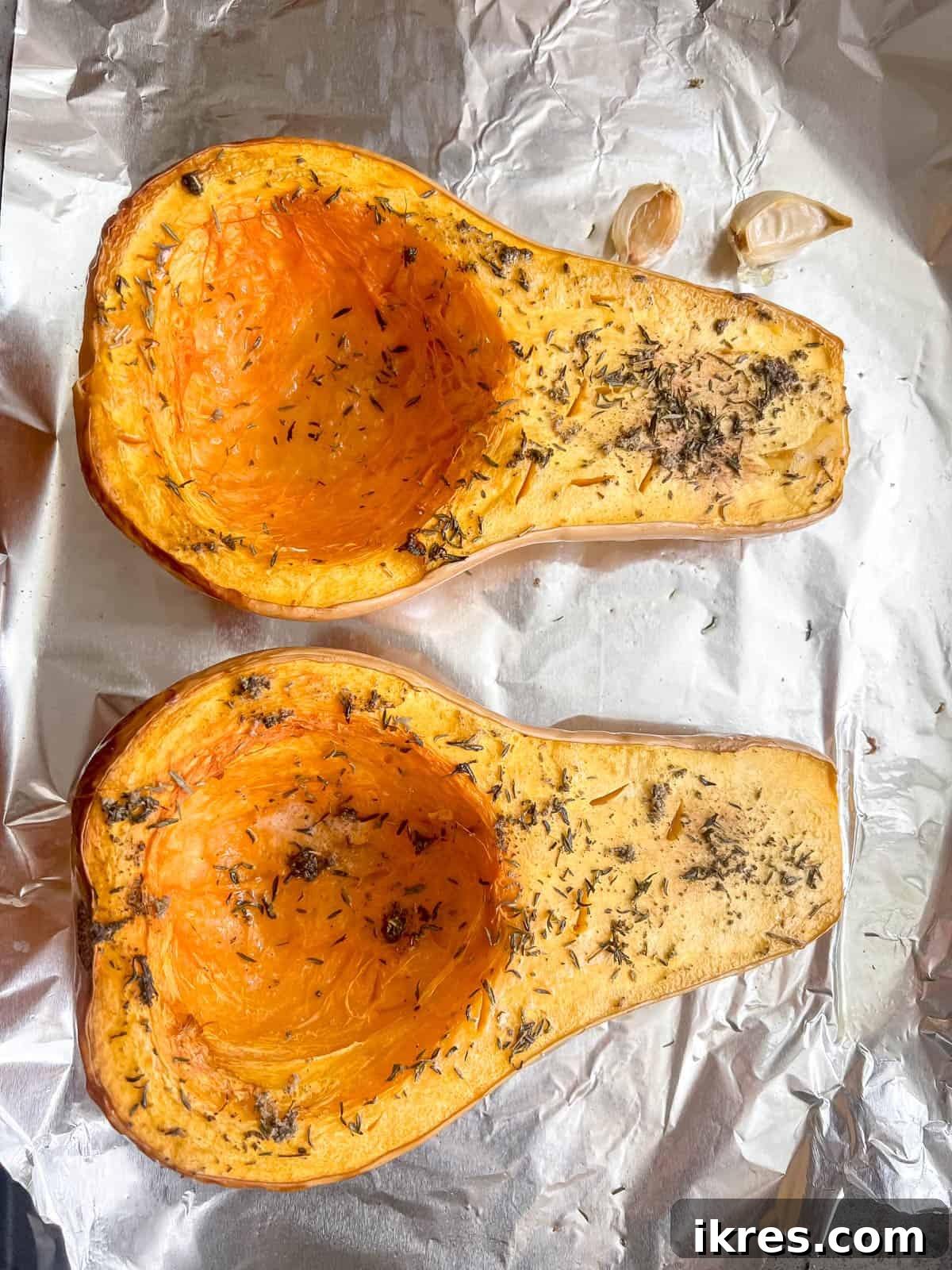 Golden Butternut Cloud 5 Perfectly roasted butternut squash halves, tender and slightly caramelized, with golden brown roasted garlic cloves alongside them in a baking pan.