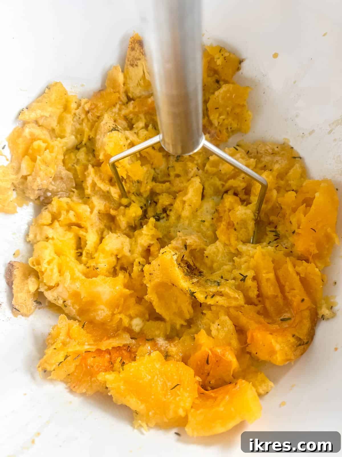 Golden Butternut Cloud 7 Smooth and creamy mashed butternut squash in a mixing bowl, showing the perfect texture after mashing, with a potato masher resting nearby.