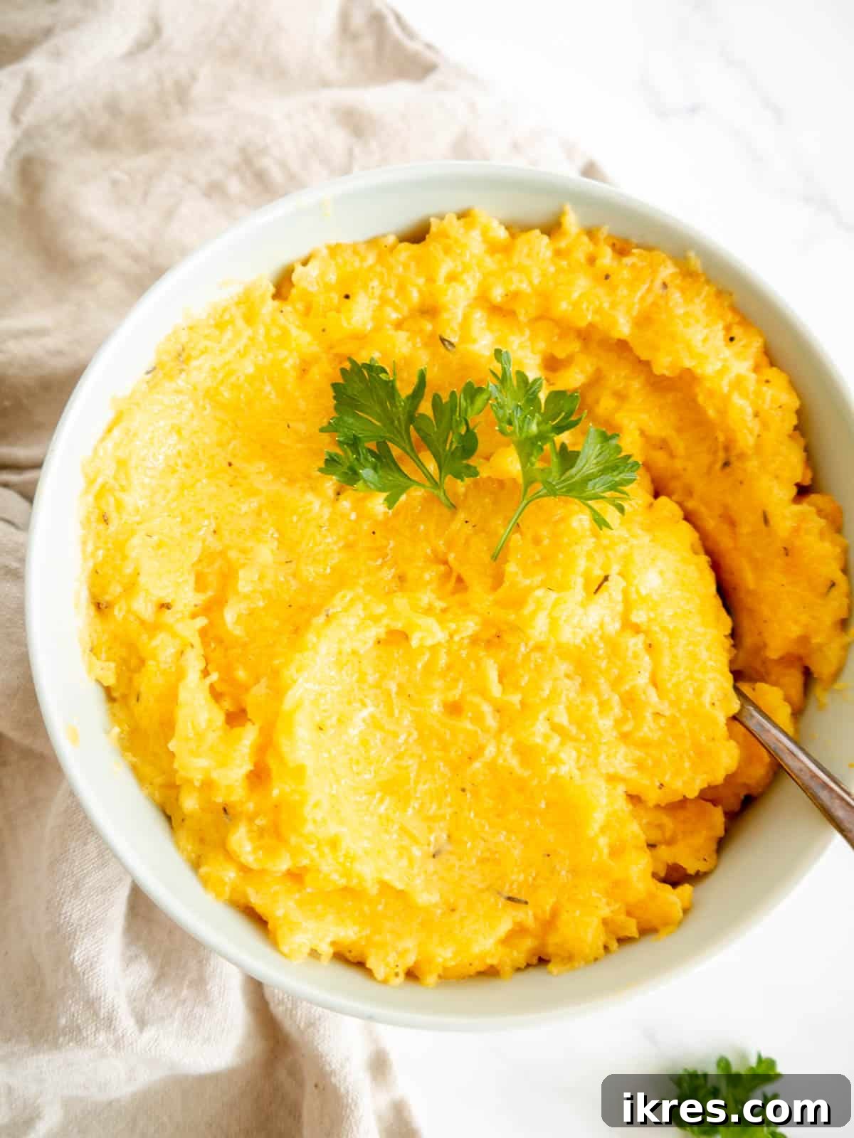 Golden Butternut Cloud 8 Close-up of creamy mashed butternut squash served in a beautiful white ceramic bowl, adorned with a fresh sprig of thyme and a spoon, ready to be enjoyed.
