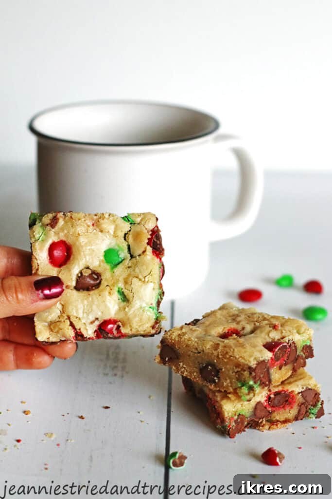 Decadent Cookie Squares 2 Festive M&M Cookie Bars on a table next to a white mug, ready for the holidays.