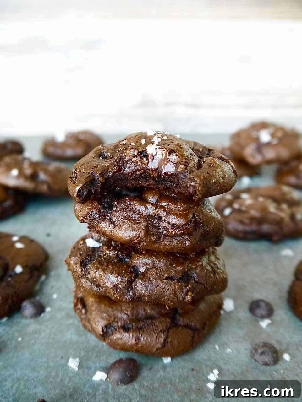Decadent Paleo Gluten-Free Double Chocolate Chip Cookies 11 A stack of four fudgy double chocolate chip cookies, garnished with sea salt, on a clean white surface.