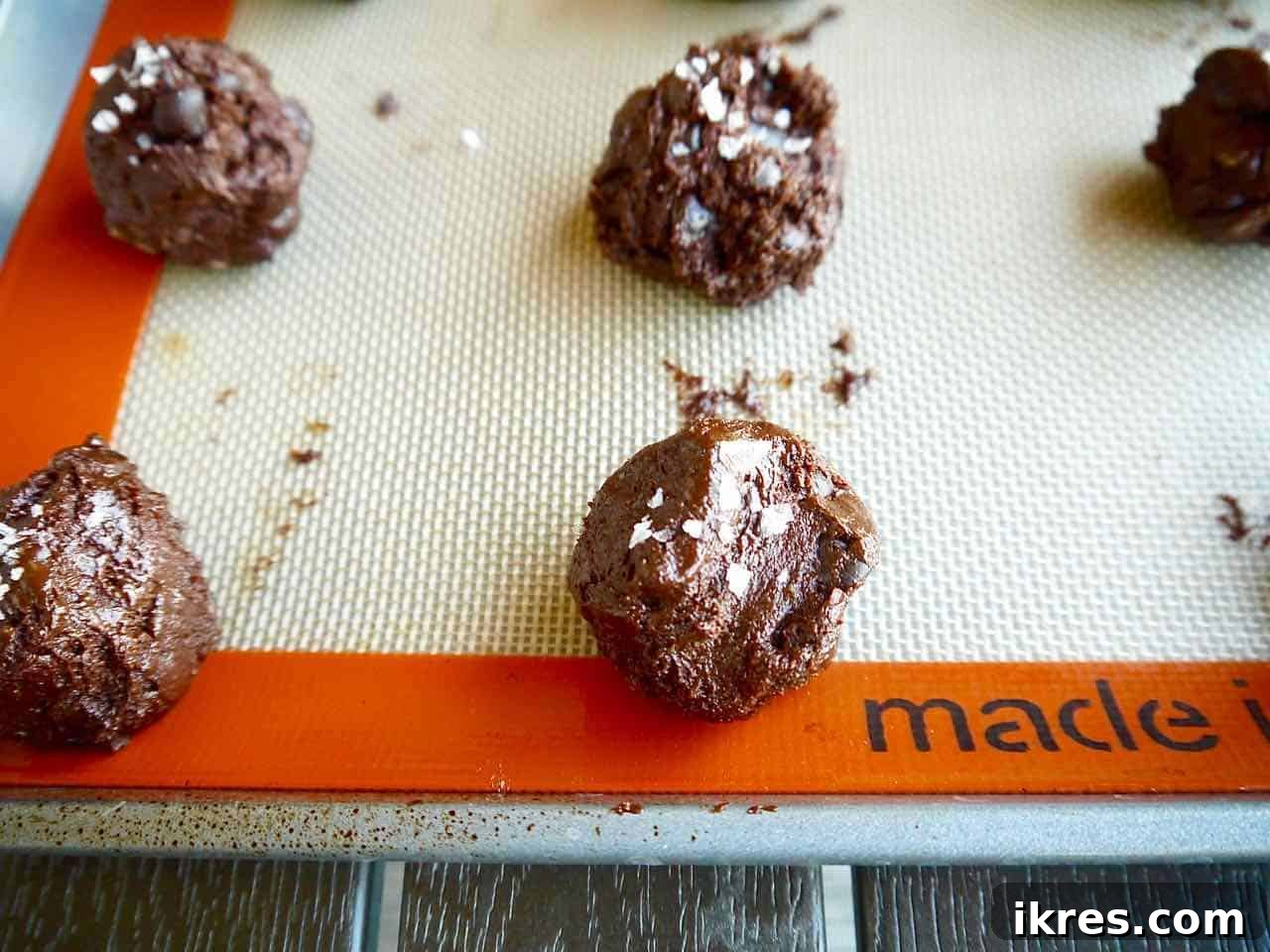 Decadent Paleo Gluten-Free Double Chocolate Chip Cookies 9 Cookie dough rolled into balls on a parchment-lined baking pan, sprinkled with sea salt.