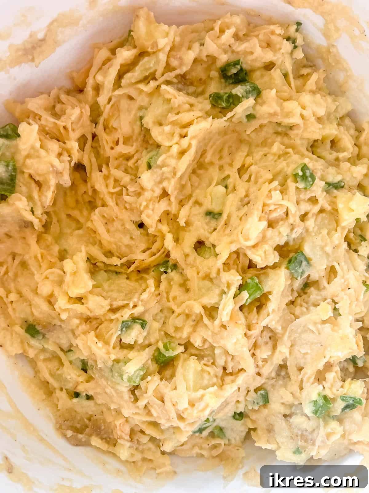 The drained shredded potatoes are being folded into the combined mashed potato and flour mixture.