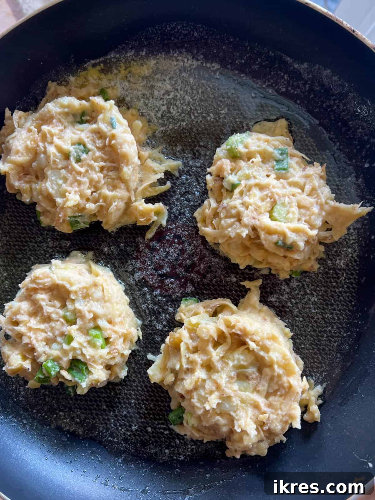 Portions of potato pancake batter cooking in a frying pan with hot avocado oil and butter, sizzling and turning golden brown.