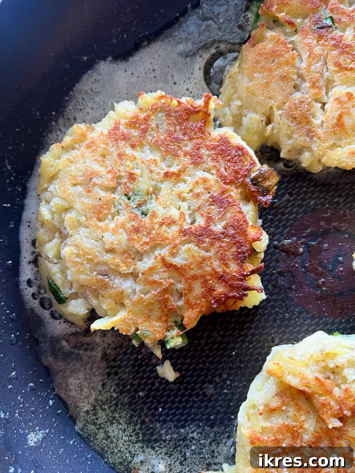 A spatula flipping a potato pancake in a frying pan, revealing a perfectly golden and crispy cooked side.