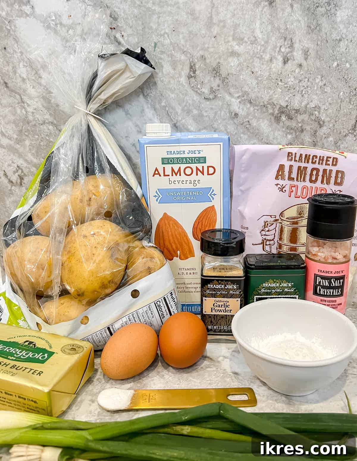 A selection of fresh ingredients laid out, including gold potatoes, butter, almond milk, eggs, green onions, and various flours, ready to be prepared for gluten-free potato pancakes.