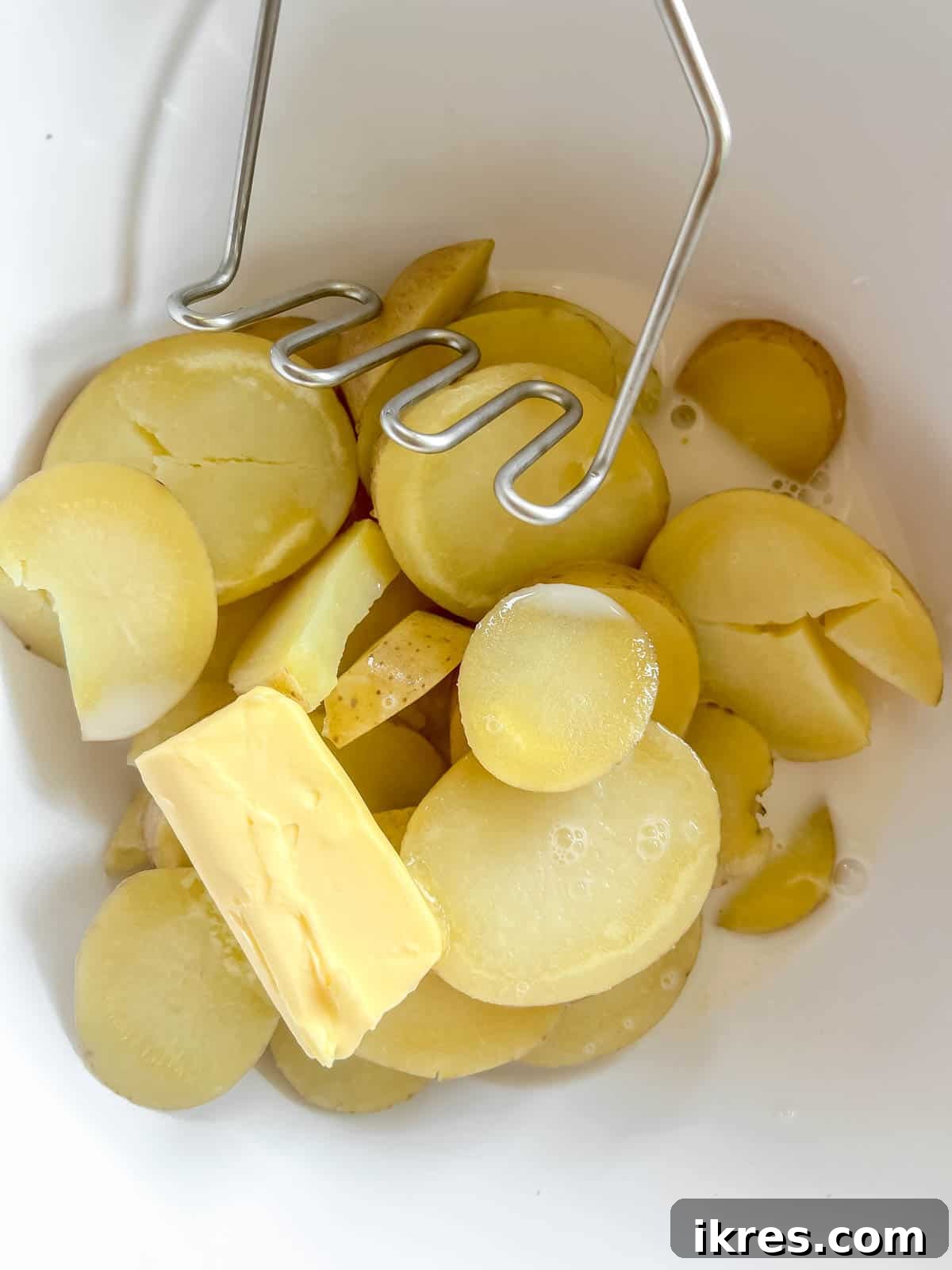 Boiled potatoes in a bowl with pats of butter and a splash of almond milk, ready to be mashed into a creamy consistency.