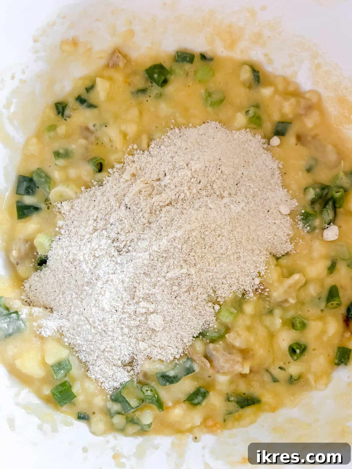 The bowl of dry flour mixture is being poured into the mashed potato mixture, ready to be combined.