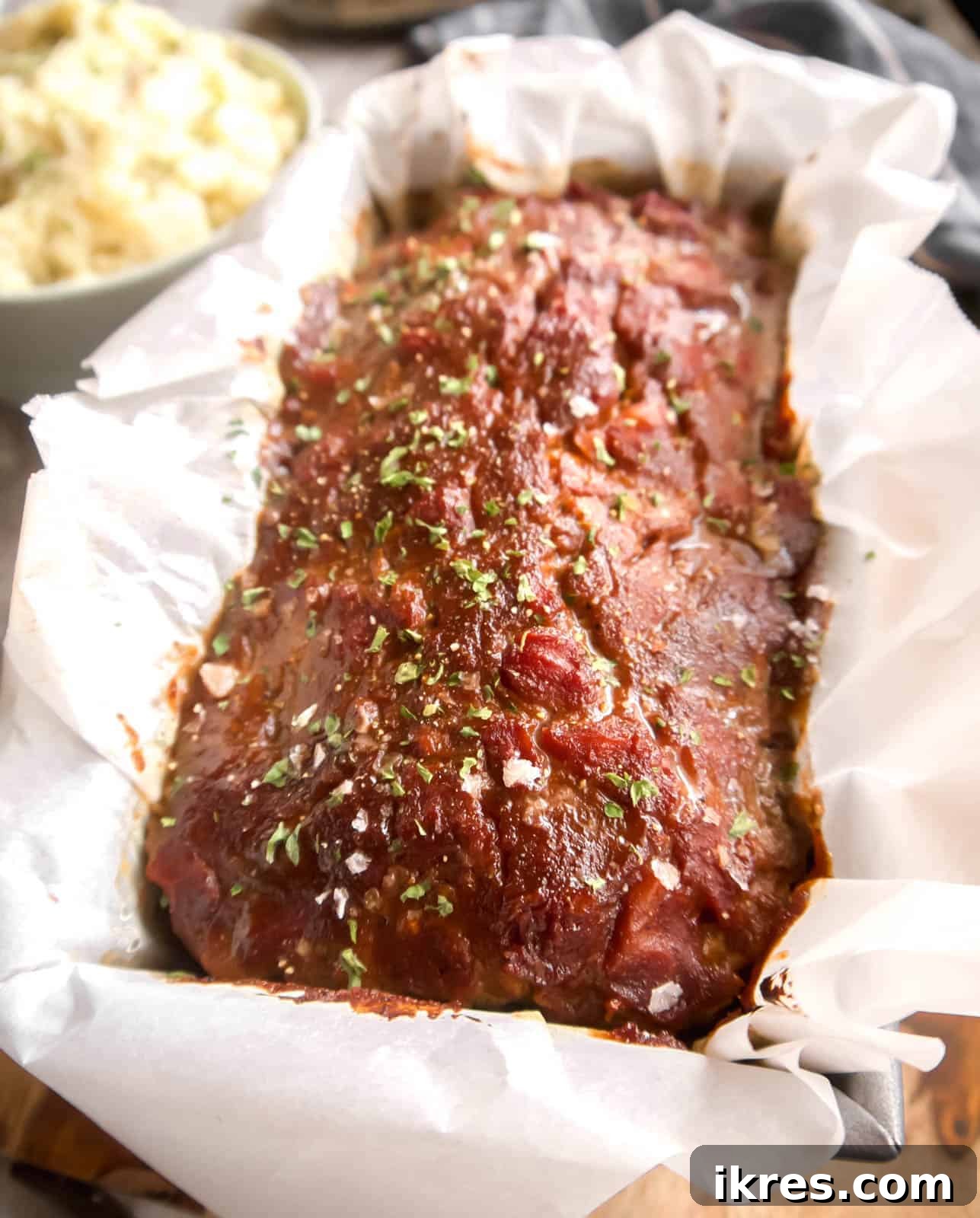 Freshly baked Paleo meatloaf emerging from the oven, generously covered in a glistening homemade sauce.