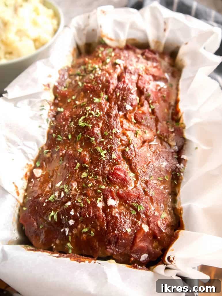 The perfectly baked paleo meatloaf, glistening with sauce, resting in its loaf pan after being removed from the oven.