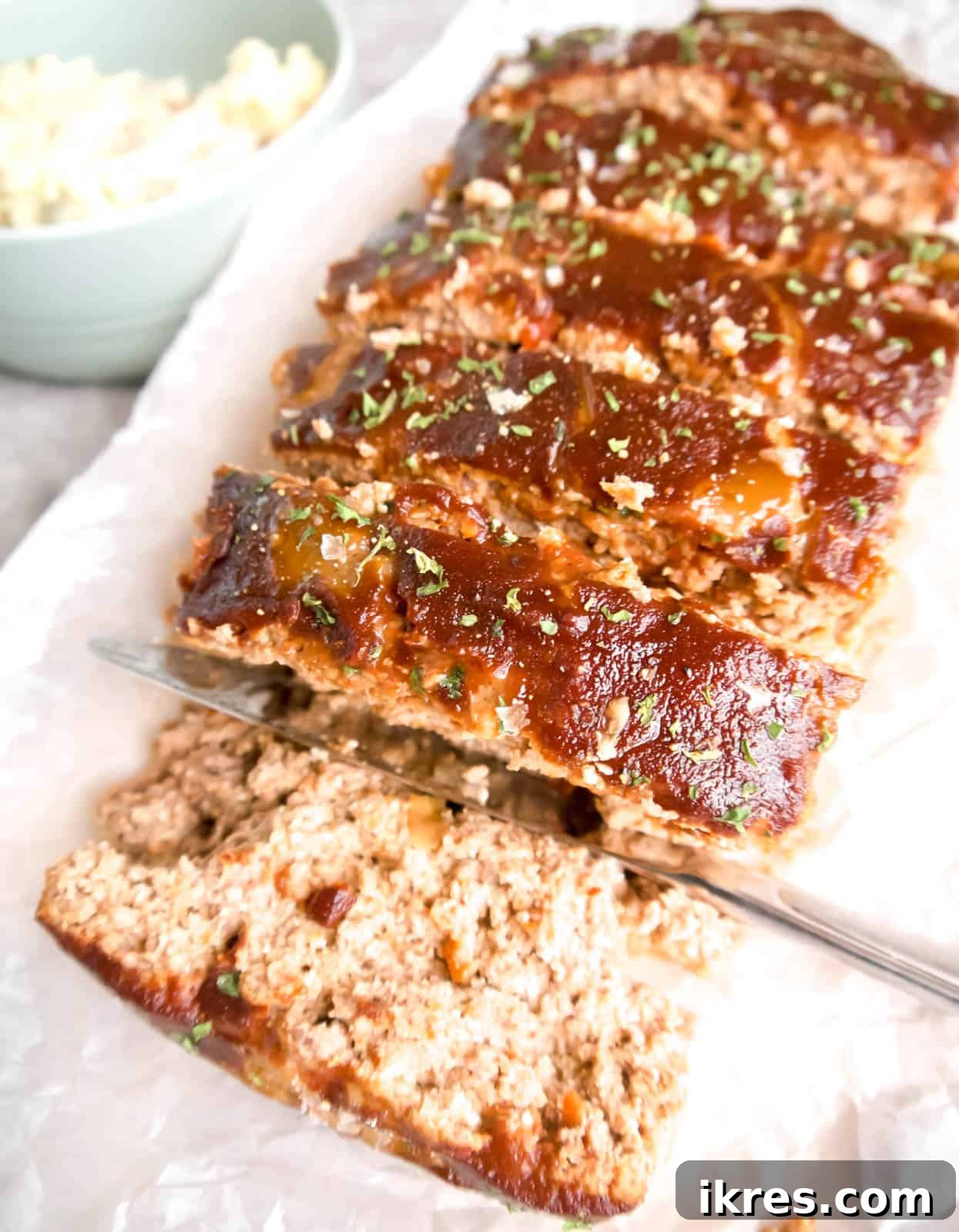 Beautifully sliced paleo meatloaf, generously coated in its savory sauce, ready for serving on a wooden cutting board.