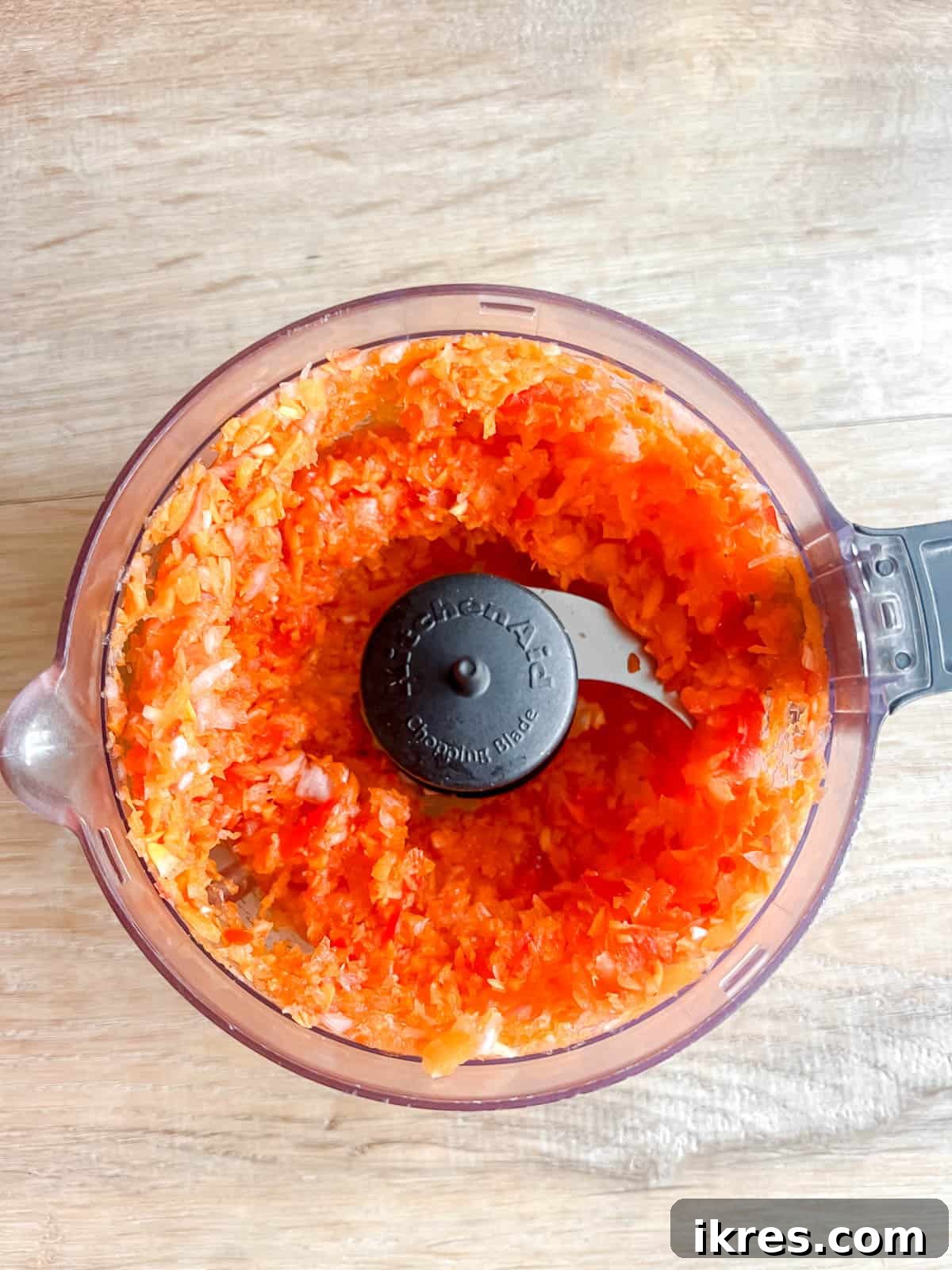 Finely minced carrots, onion, garlic, and red pepper within a food processor bowl.