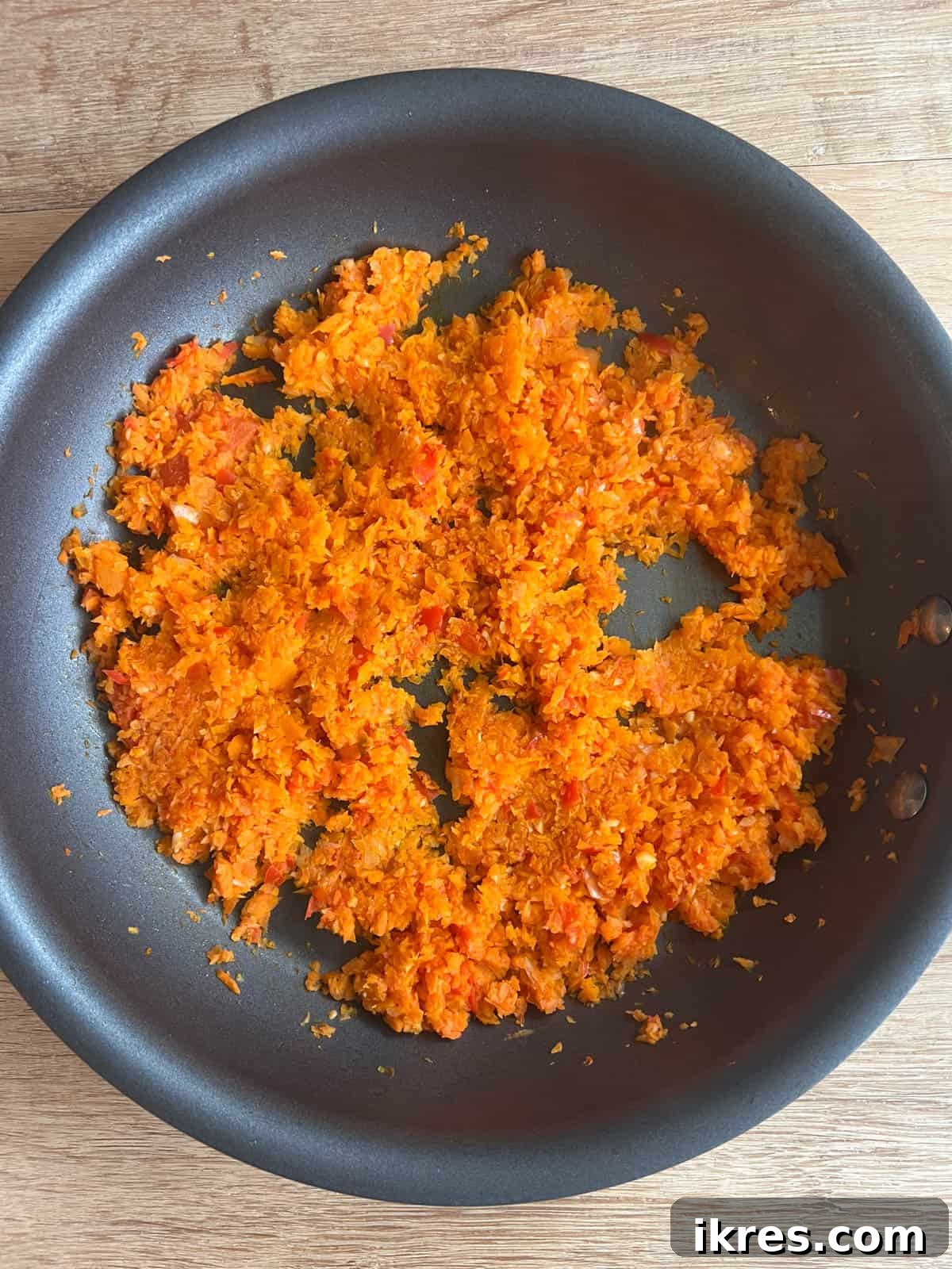 Sautéed mixture of garlic, onion, red pepper, and carrot in a pan, lightly browned and fragrant.