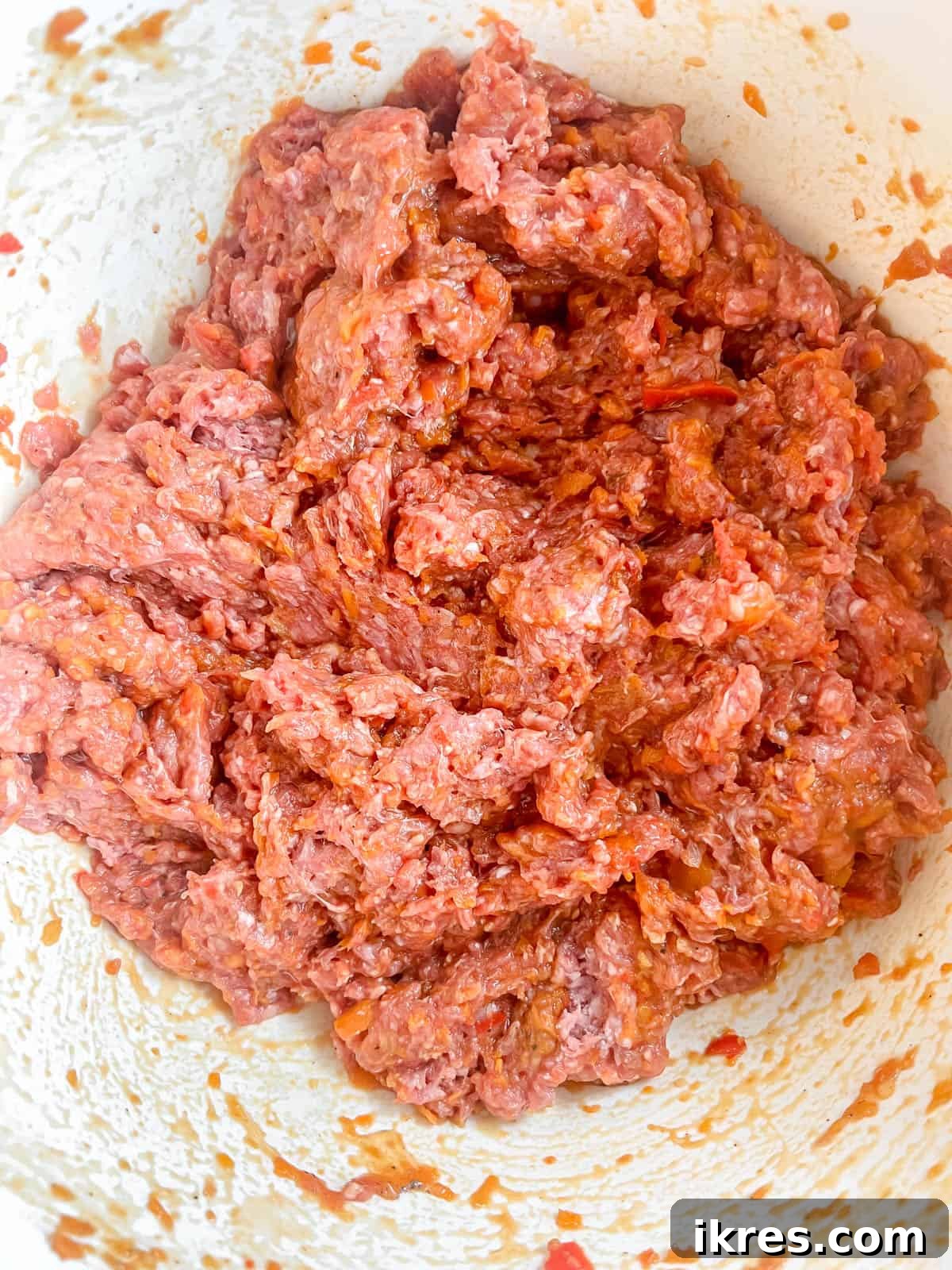 The unbaked paleo meatloaf mixture pressed evenly into a parchment-lined loaf tin, with reserved sauce.