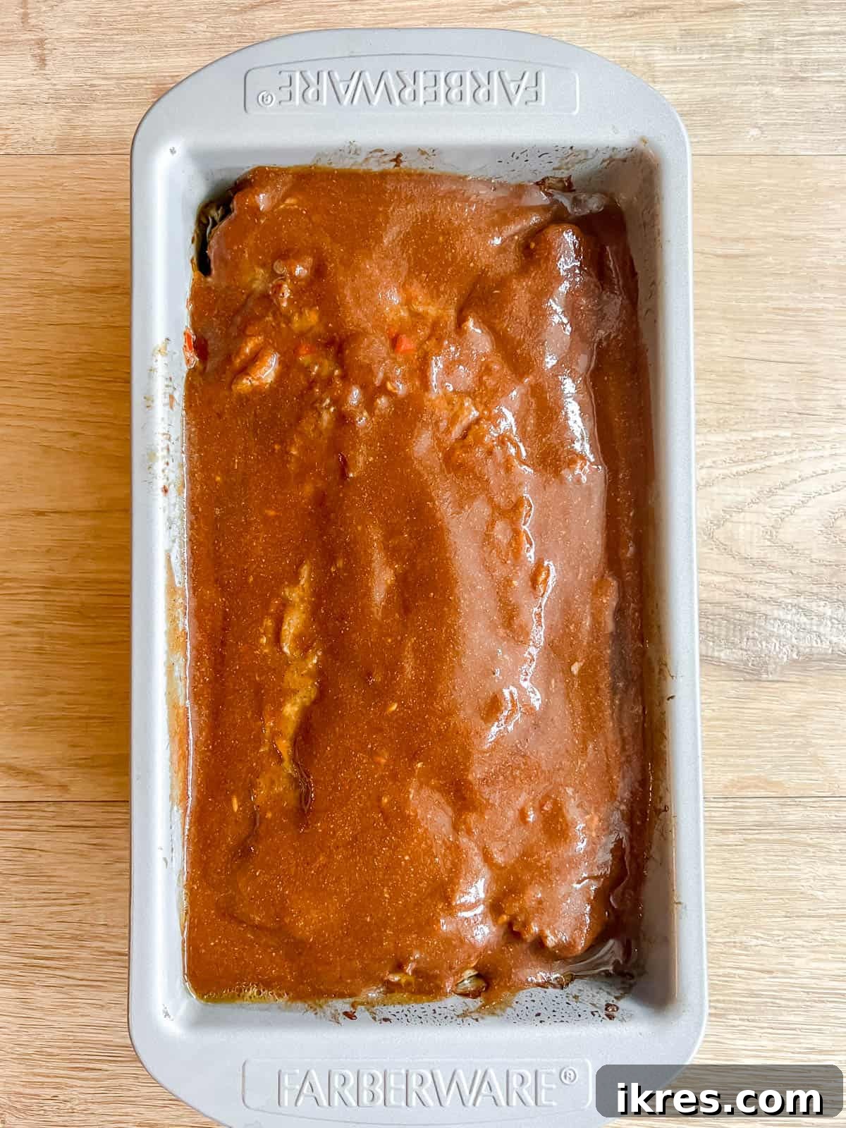 Partially baked paleo meatloaf removed from the oven, with the remaining homemade sauce being spread over its top surface.