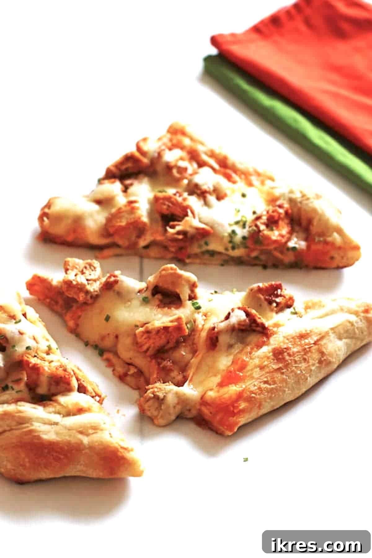 Ultimate Homemade Buffalo Chicken Pizza 2 Pizza slices covered with cheese, chicken and chicken wing sauce on a white table.