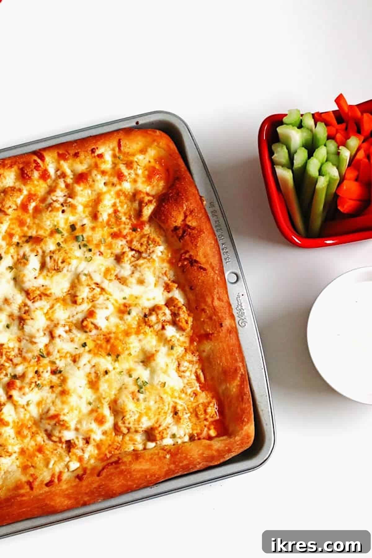 Ultimate Homemade Buffalo Chicken Pizza 4 Buffalo Chicken Pizza in baking pan with carrots, celery and blue cheese dressing on the side.