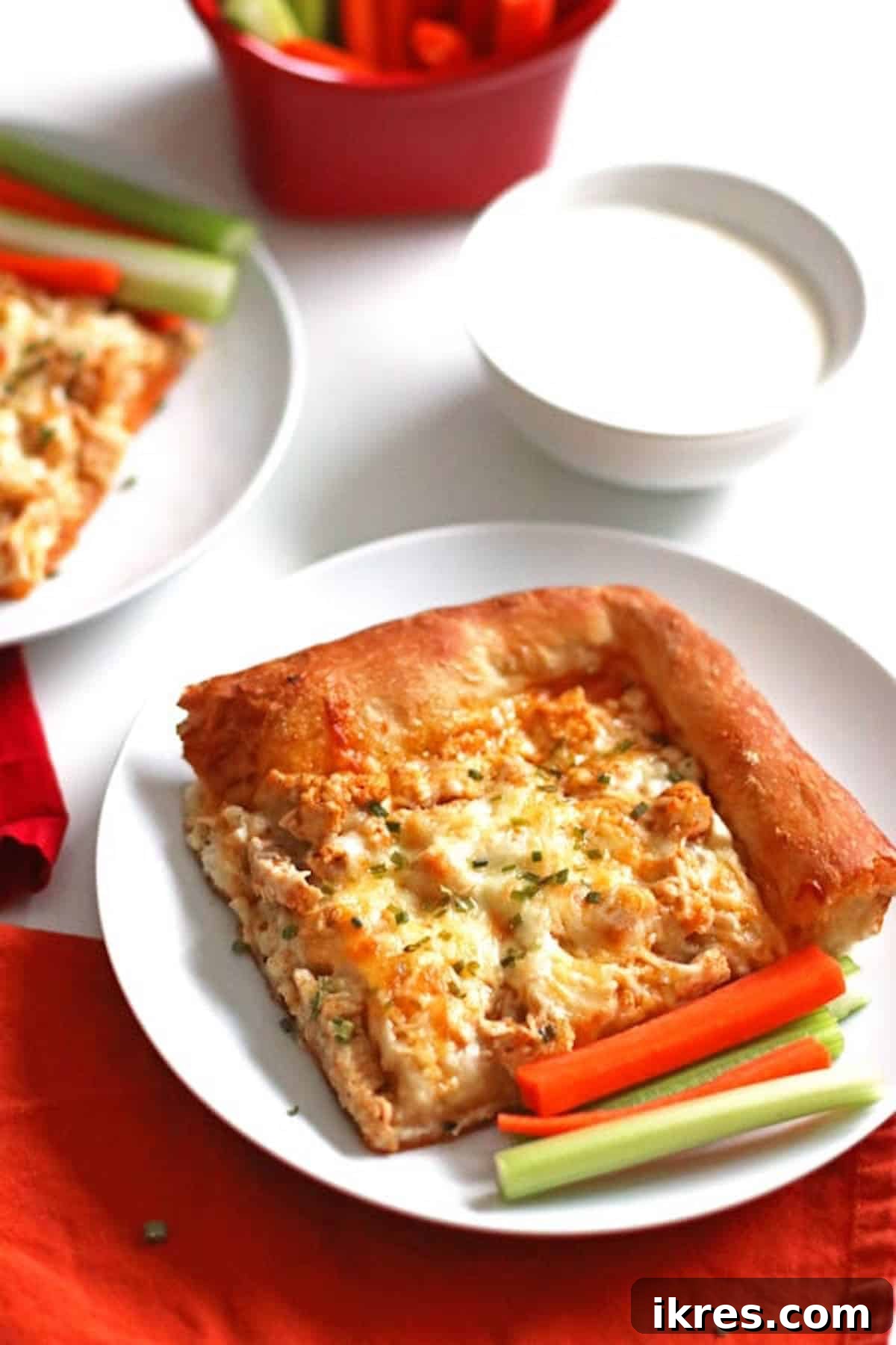 Ultimate Homemade Buffalo Chicken Pizza 7 A corner piece of buffalo chicken pizza on a white plate with celery and carrot sticks.