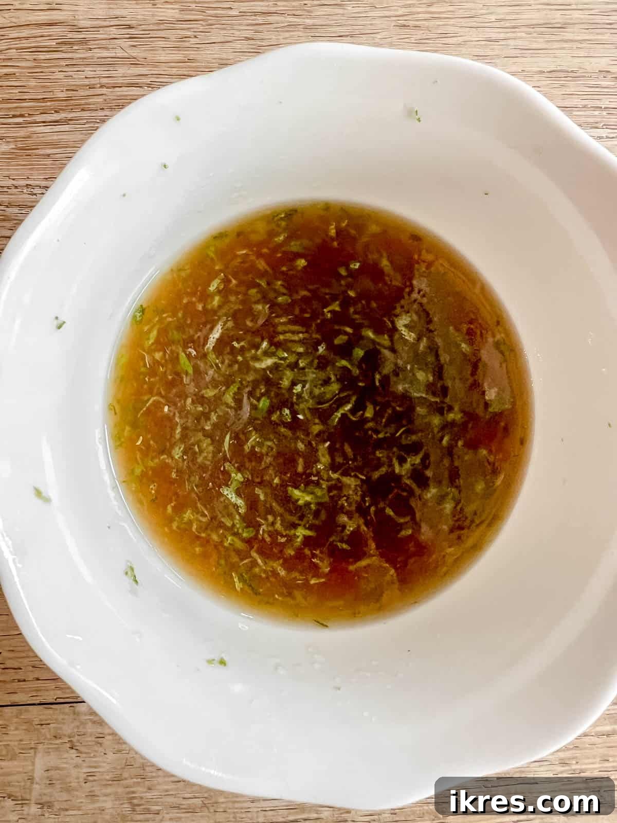 A bowl containing a freshly mixed blend of maple syrup, lime juice, and lime zest, forming the vibrant maple lime sauce.