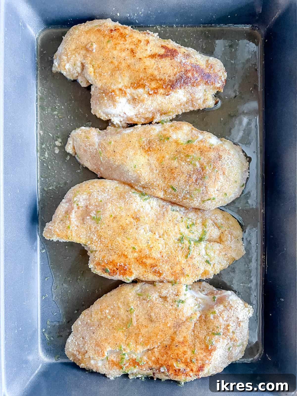 Seared and breaded chicken breasts carefully placed in a baking pan, ready to be covered generously with the maple lime sauce before baking.
