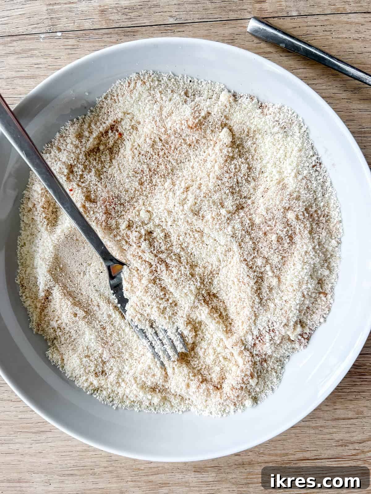 A bowl containing a mixed blend of almond flour, cinnamon, nutmeg, paprika, salt, and pepper, forming the dry breading mixture for chicken.
