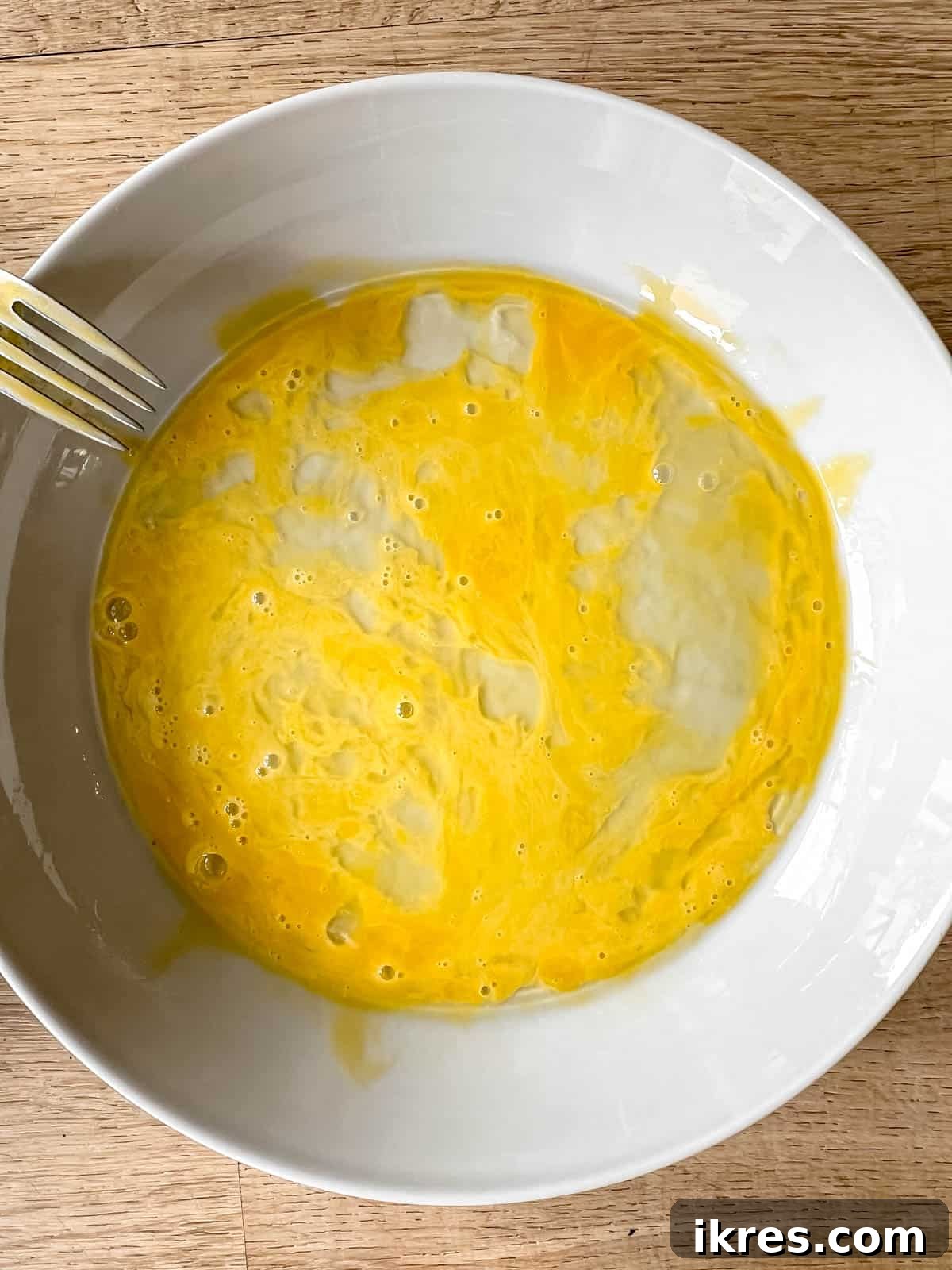A separate bowl filled with a well-whisked egg, prepared as the wet component for breading the chicken.