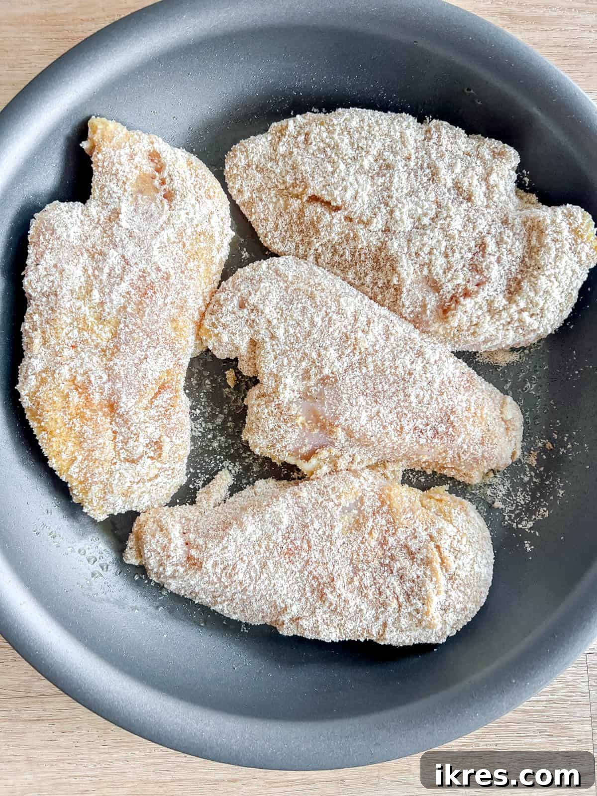 Breaded chicken breasts arranged in a large frying pan, lightly browning on one side in olive oil.