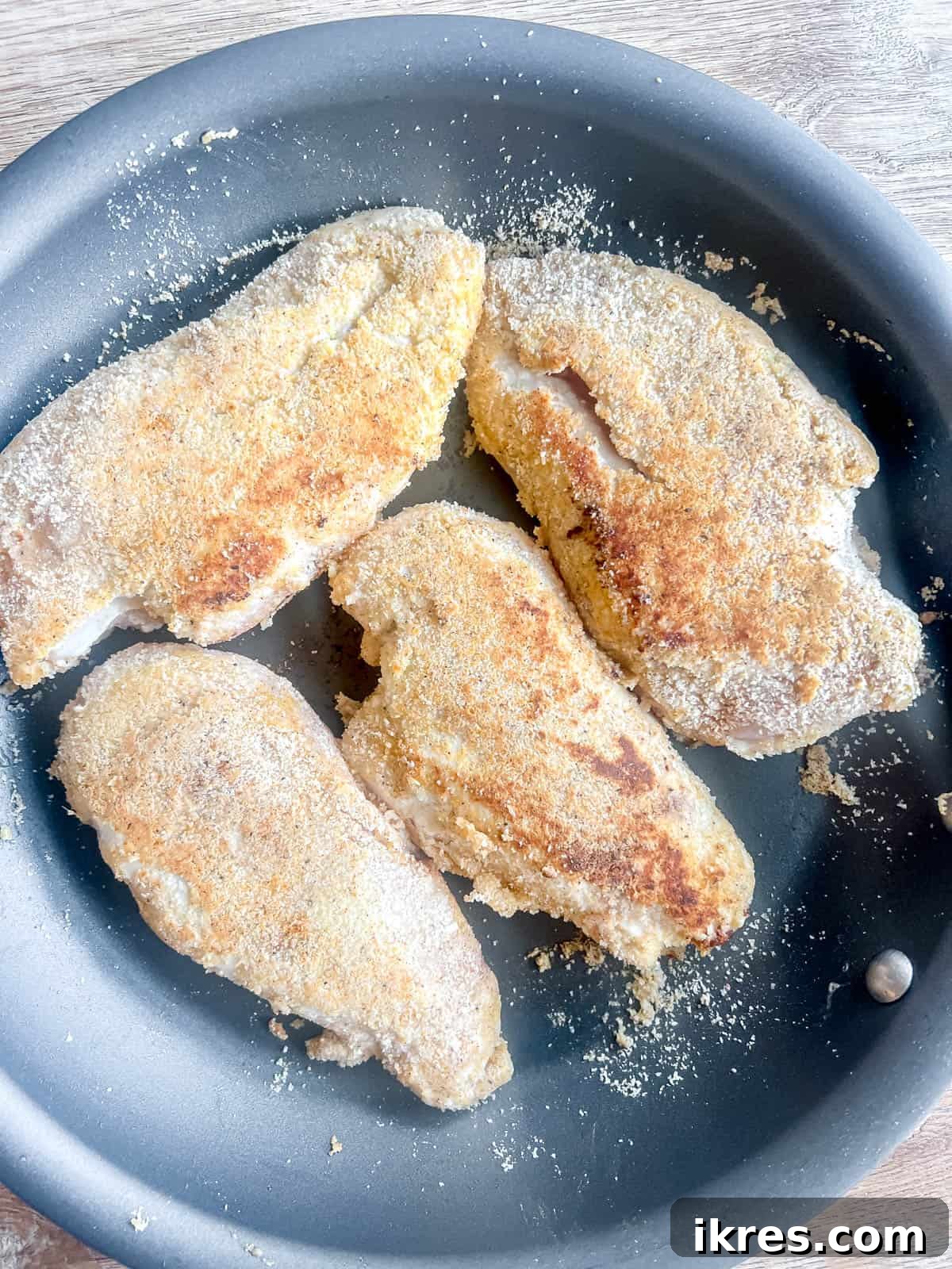 Flipped breaded chicken breasts continuing to brown on the second side in the frying pan, achieving an even golden crust.