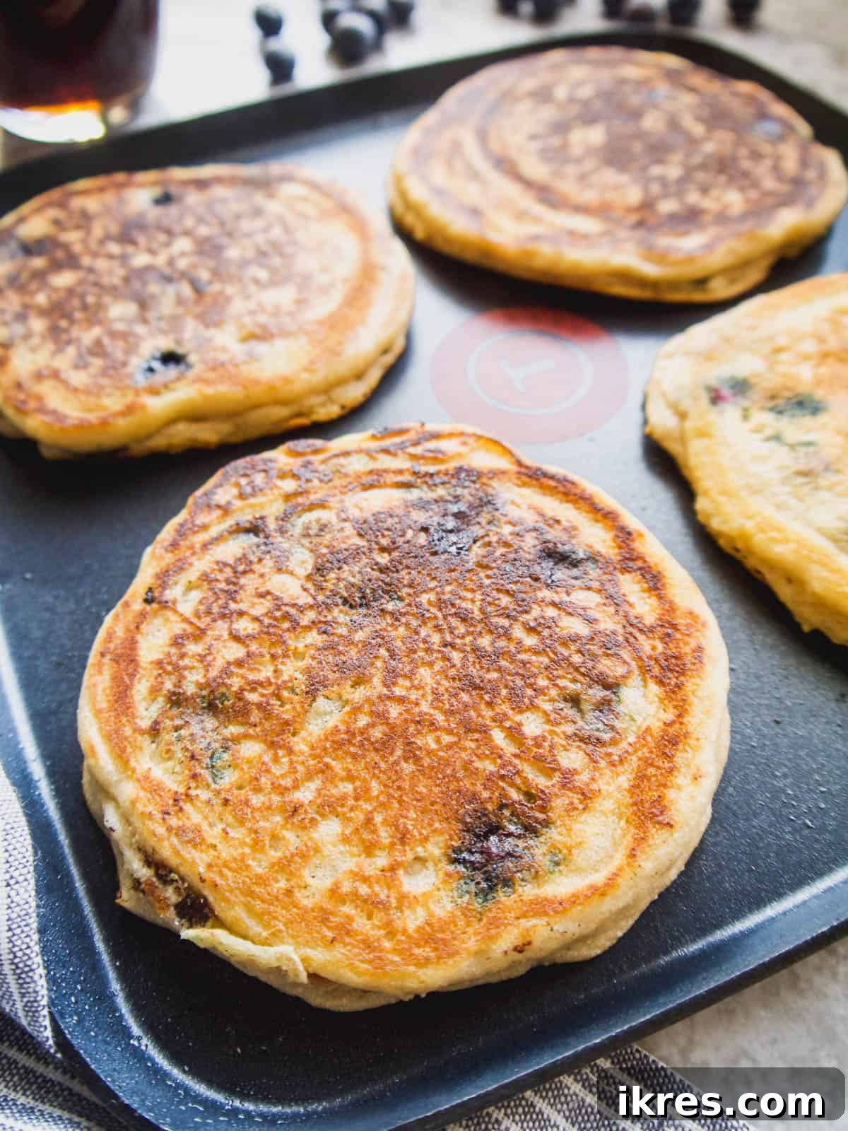 Fluffy Paleo Blueberry Pancakes 11 Paleo blueberry pancakes cooking on a griddle, showing bubbles forming on the surface.