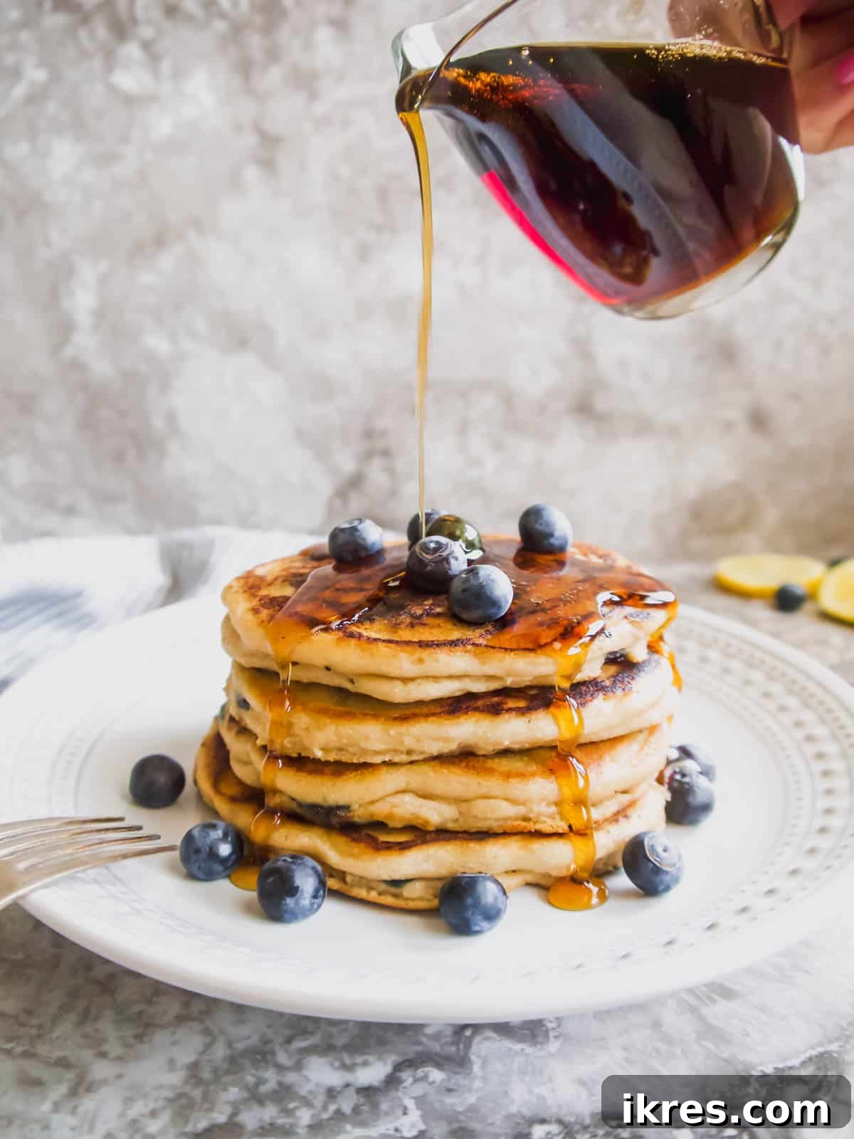 Fluffy Paleo Blueberry Pancakes 3 Golden maple syrup being generously poured over a stack of fluffy Paleo blueberry pancakes.
