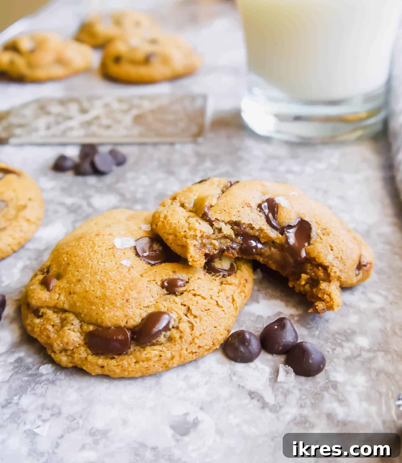 Two soft and chewy almond flour chocolate chip cookies, one with a bite taken out, stacked delicately on a wooden surface.