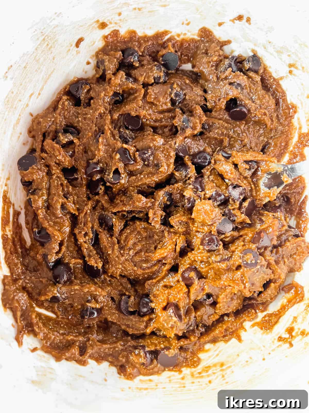 A bowl filled with freshly mixed Paleo chocolate chip cookie dough, featuring visible dairy-free chocolate chips integrated throughout.