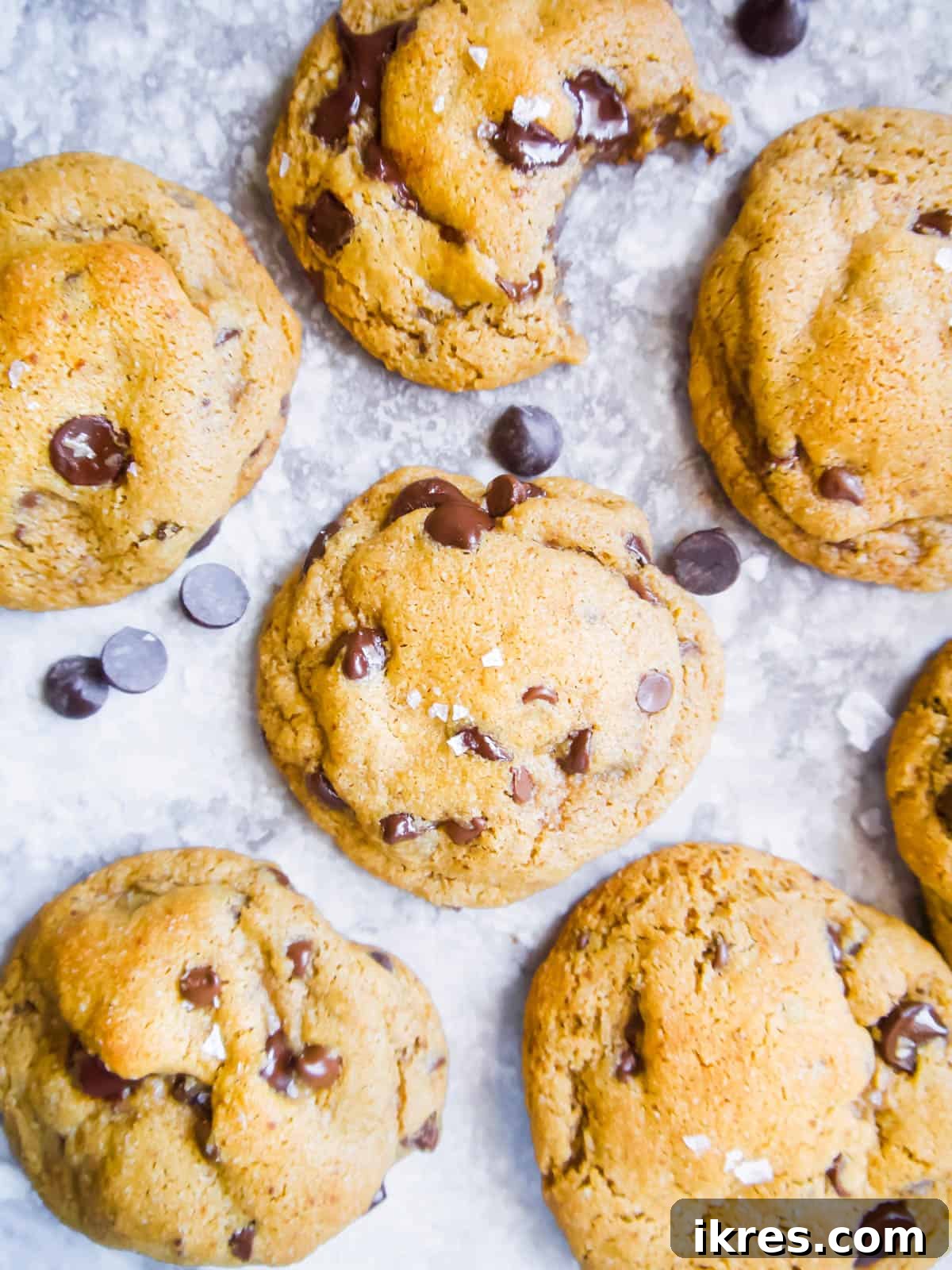 A delectable arrangement of several freshly baked Paleo chocolate chip cookies made with coconut oil, artfully placed on a table alongside a scattering of dairy-free chocolate chips.