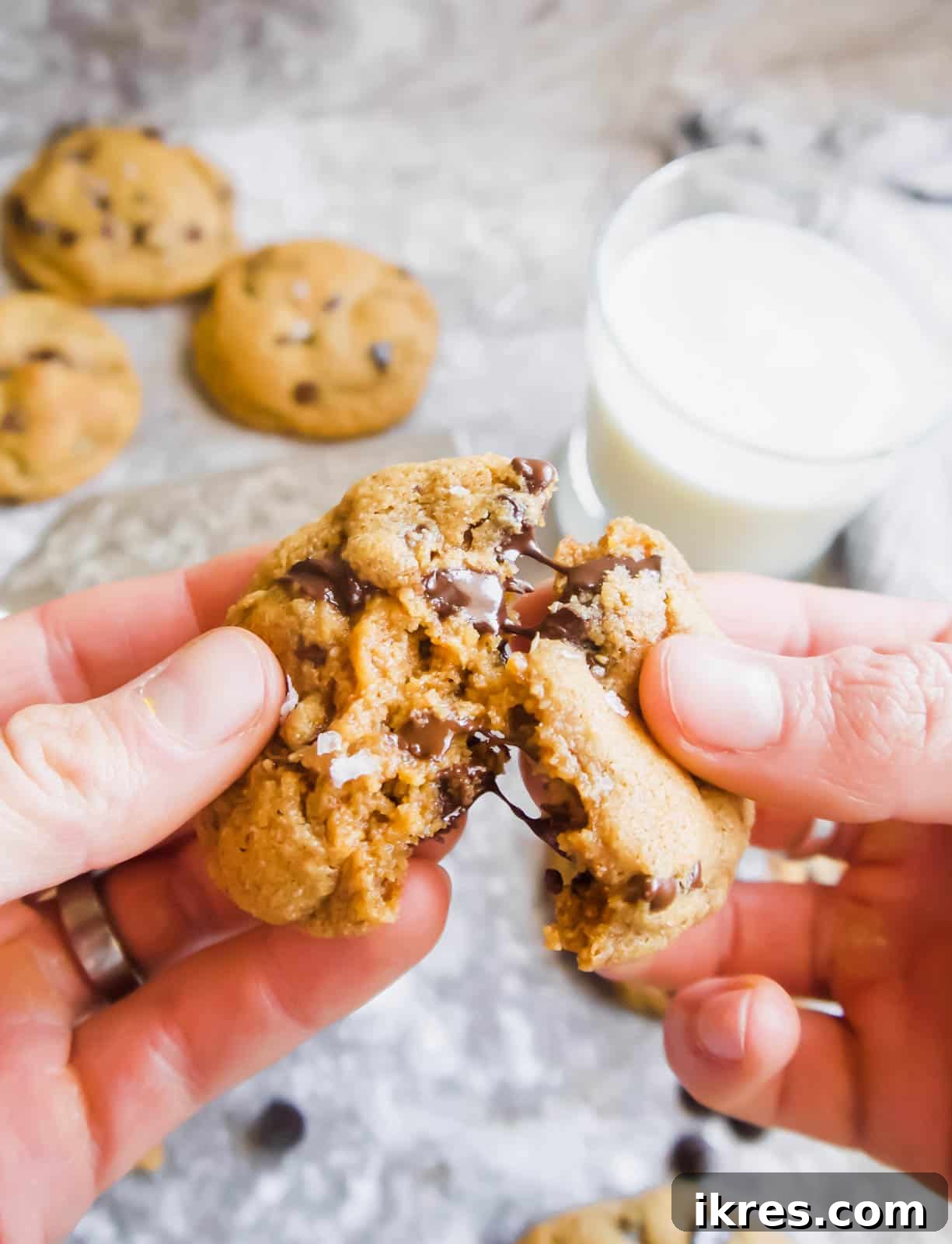 Grain and Dairy Free Paleo Chocolate Chip Cookies 10 Hands breaking a coconut oil chocolate chip cookie in half, revealing its soft, chewy center.
