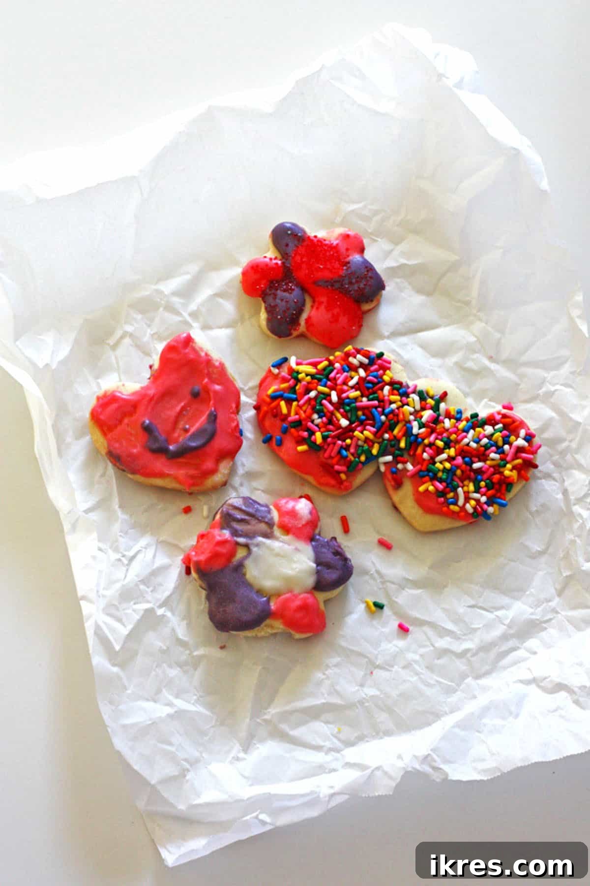 Heart-shaped sugar cookies, whimsically adorned with sprinkles, resting on a crumpled piece of parchment paper.
