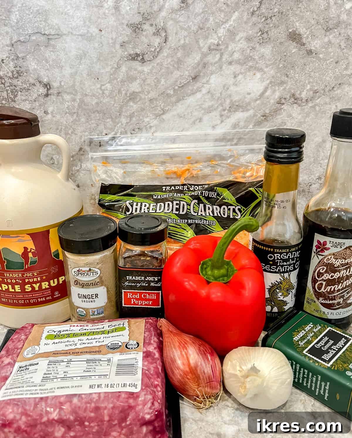 A flat lay photograph showcasing all the fresh ingredients needed for Healthy Korean Ground Beef Bowls, including garlic, green onions, red pepper, carrots, ground beef, coconut aminos, maple syrup, sesame oil, and spices.