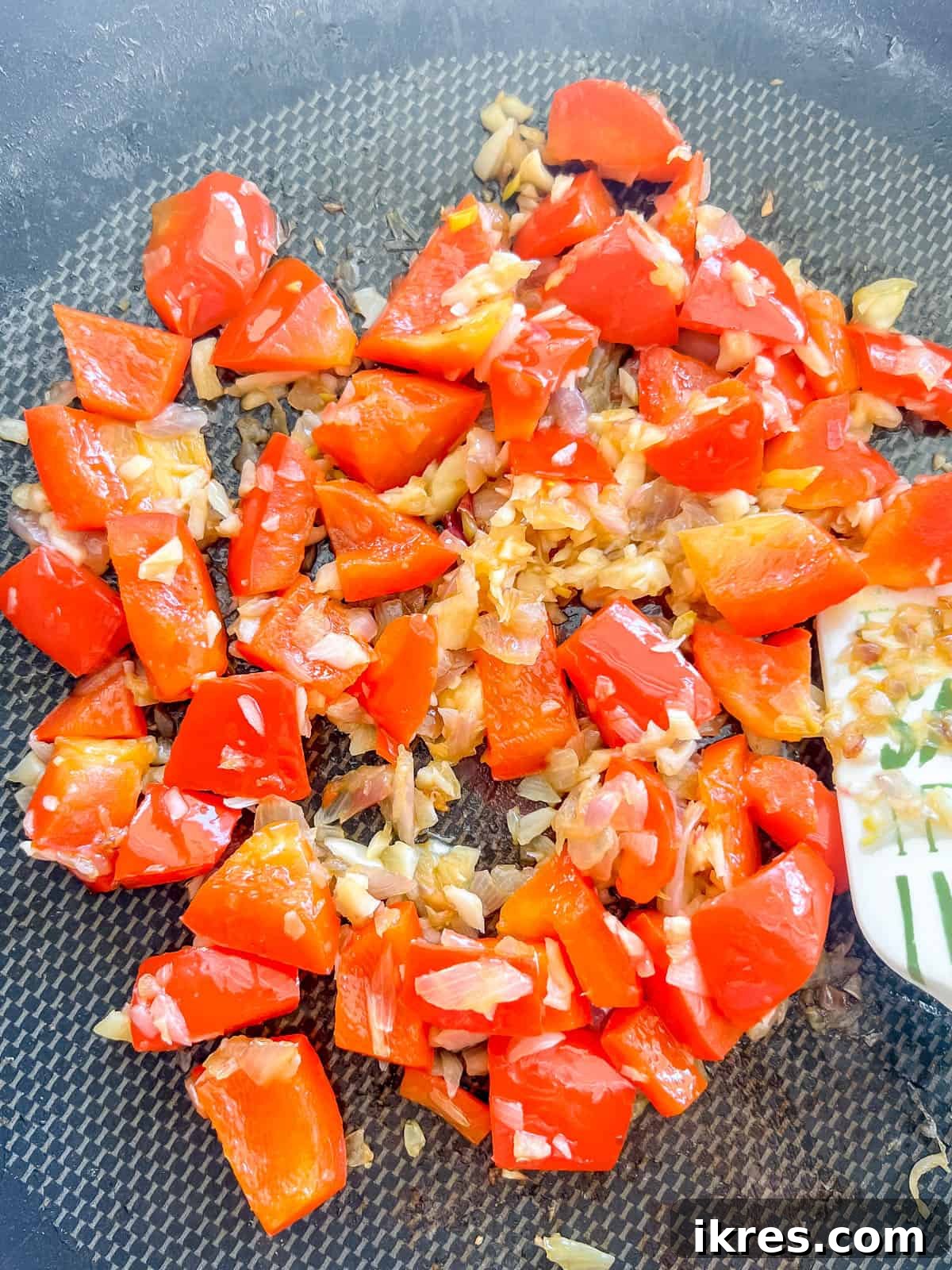 Diced red pepper, minced garlic, and sliced green onions sizzling in a frying pan with sesame oil.