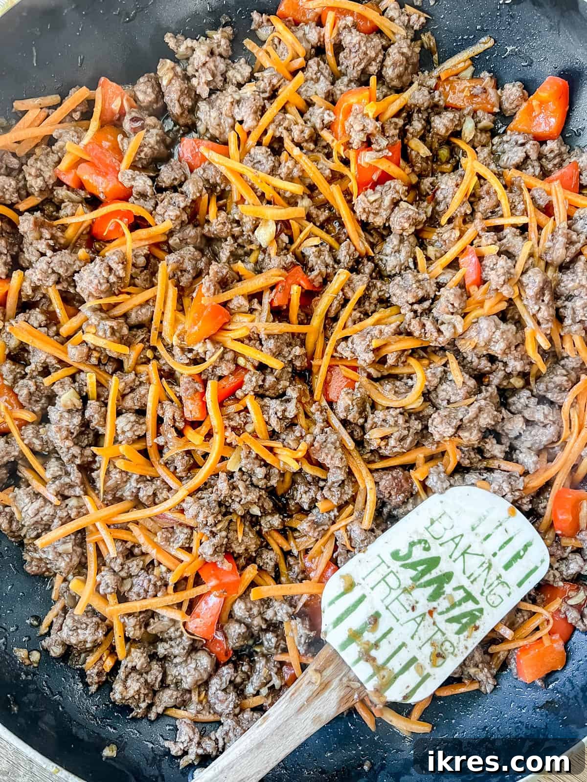 Shredded carrots and the prepared coconut aminos sauce being added to the browned ground beef in the pan.