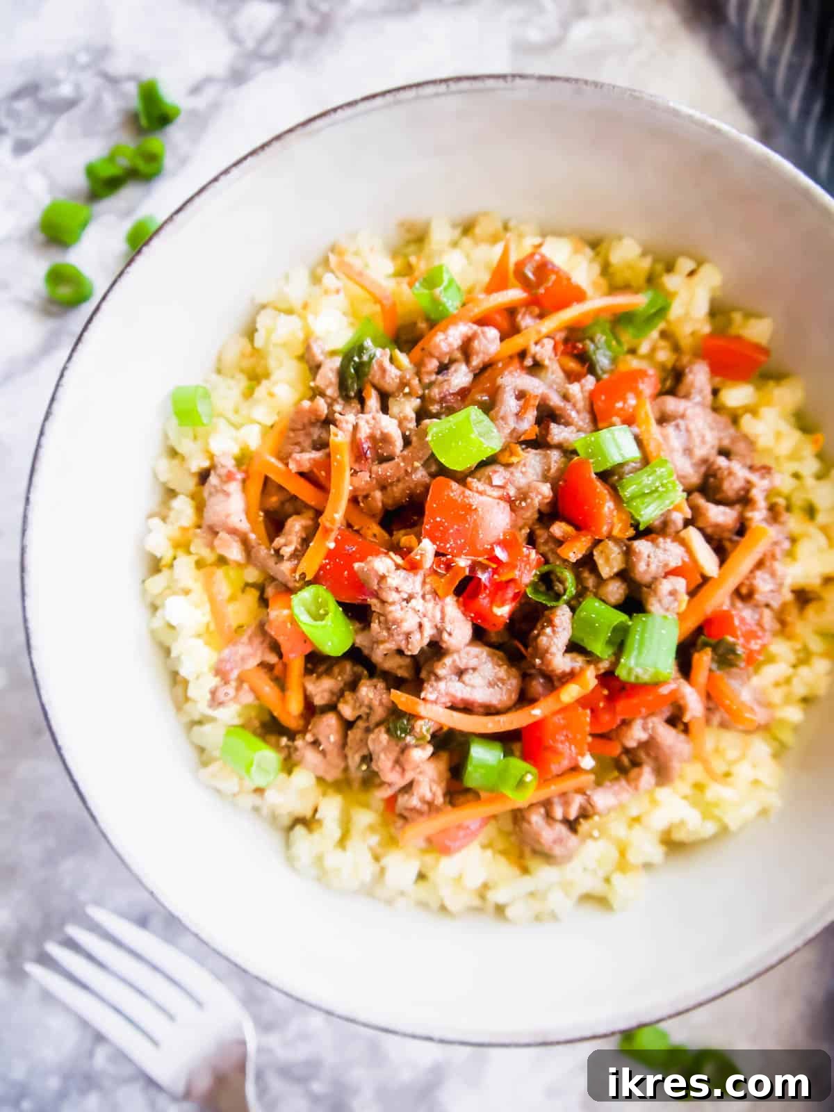 A delicious Paleo and Whole30 Korean Beef Bowl served over a bed of cauliflower rice, garnished with green onions and sesame seeds.