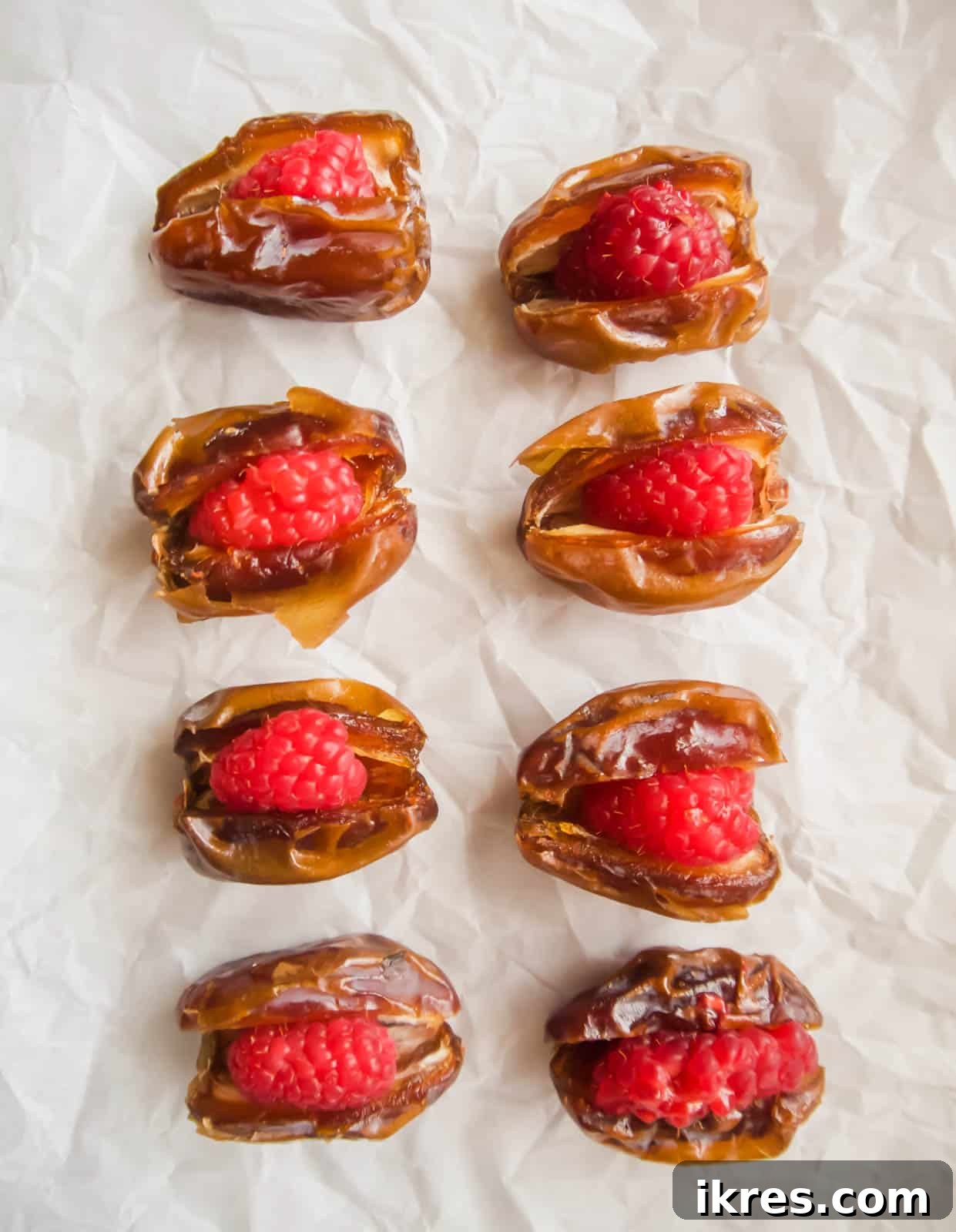 Blissful Bacon Wrapped Raspberry Date Bites 6 Medjool dates, each carefully stuffed with a single fresh raspberry, arranged on a baking sheet.