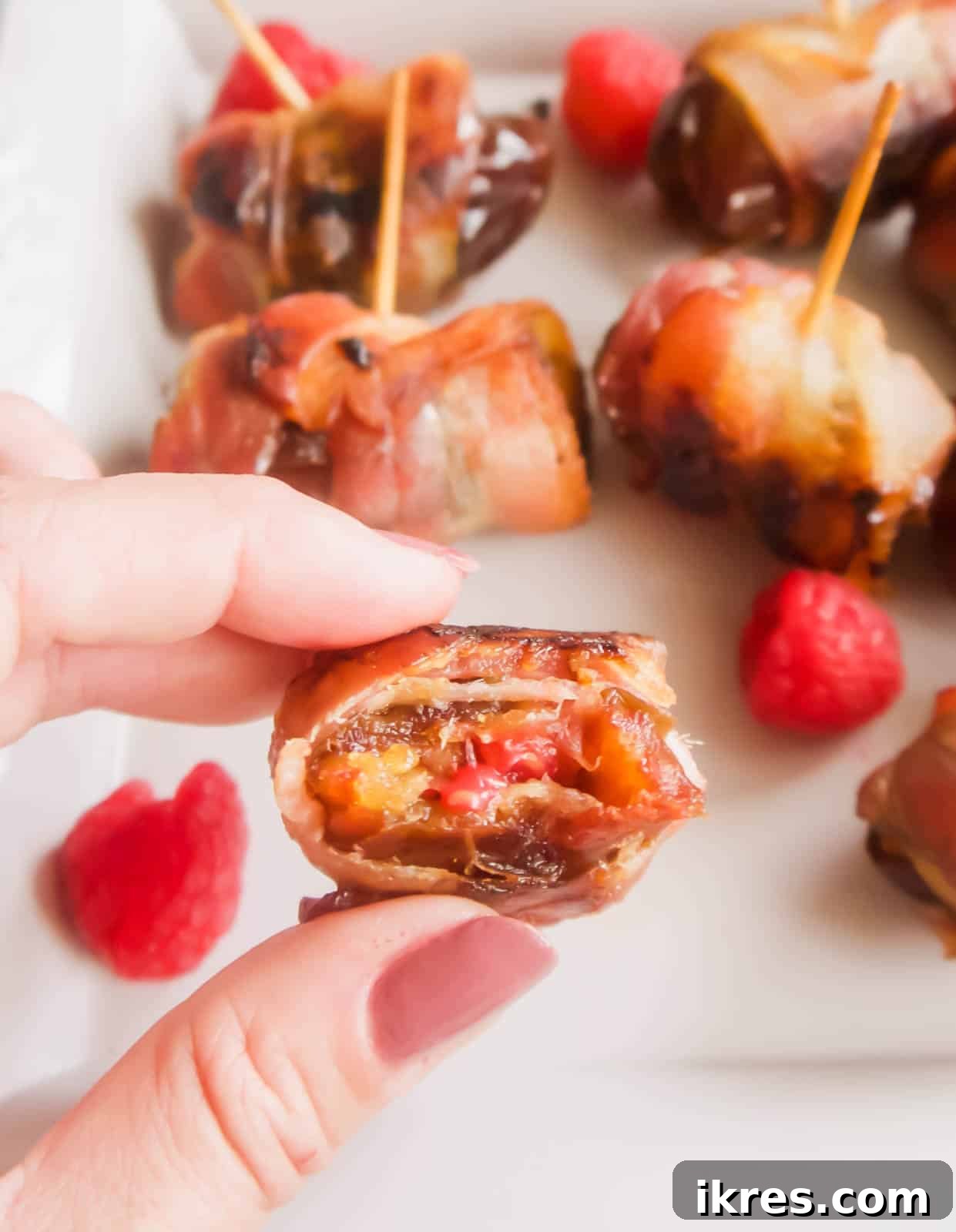 Blissful Bacon Wrapped Raspberry Date Bites 9 A perfectly cooked raspberry stuffed date wrapped in crispy bacon, with a bite taken out, revealing the soft, jammy raspberry interior.