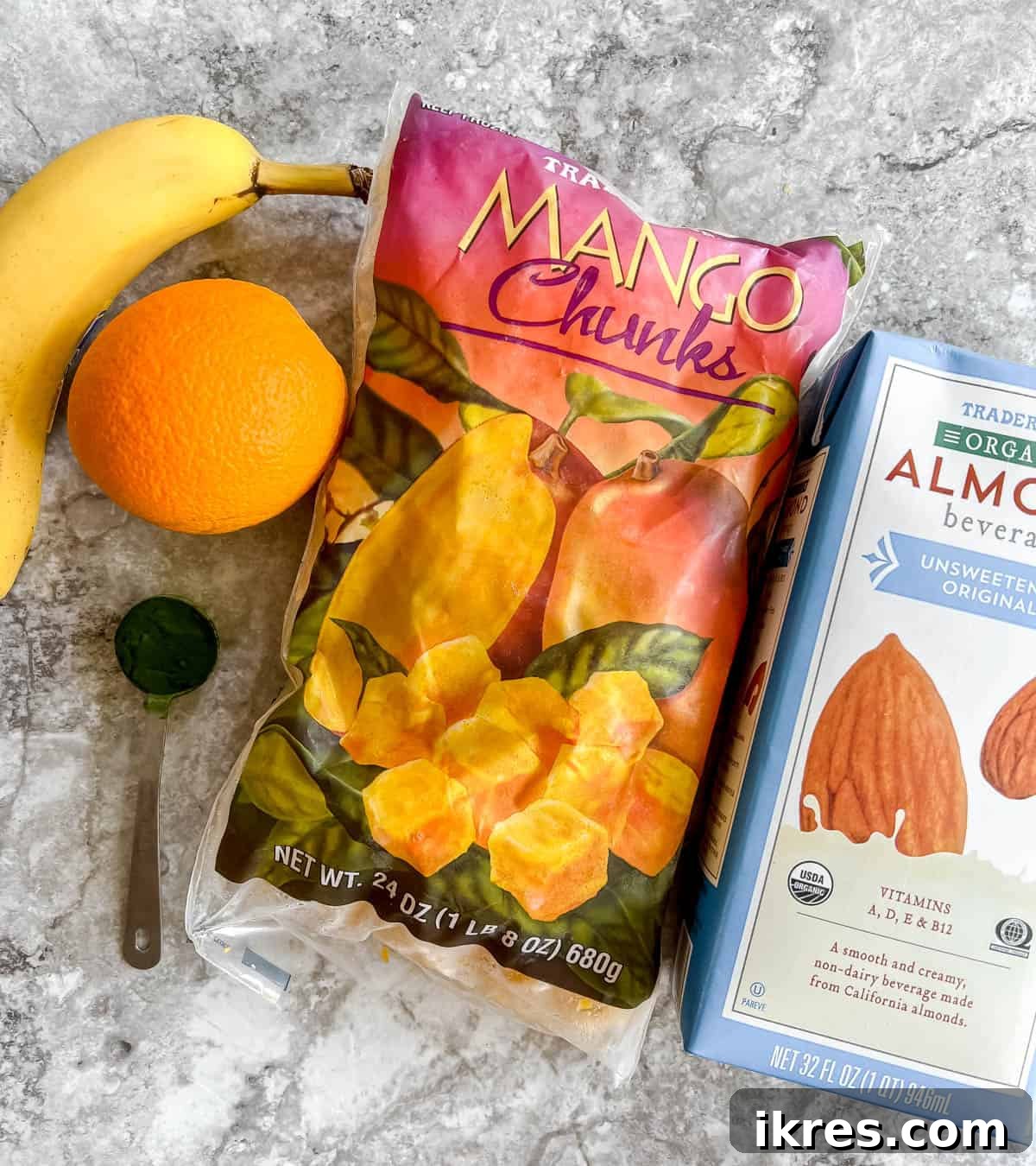 Sunrise Spirulina Fusion 4 A neatly arranged collection of fresh ingredients for a spirulina smoothie, including a bright orange, a ripe banana, a bowl of frozen mango chunks, a container of spirulina powder, and a carton of almond milk, all ready for blending.