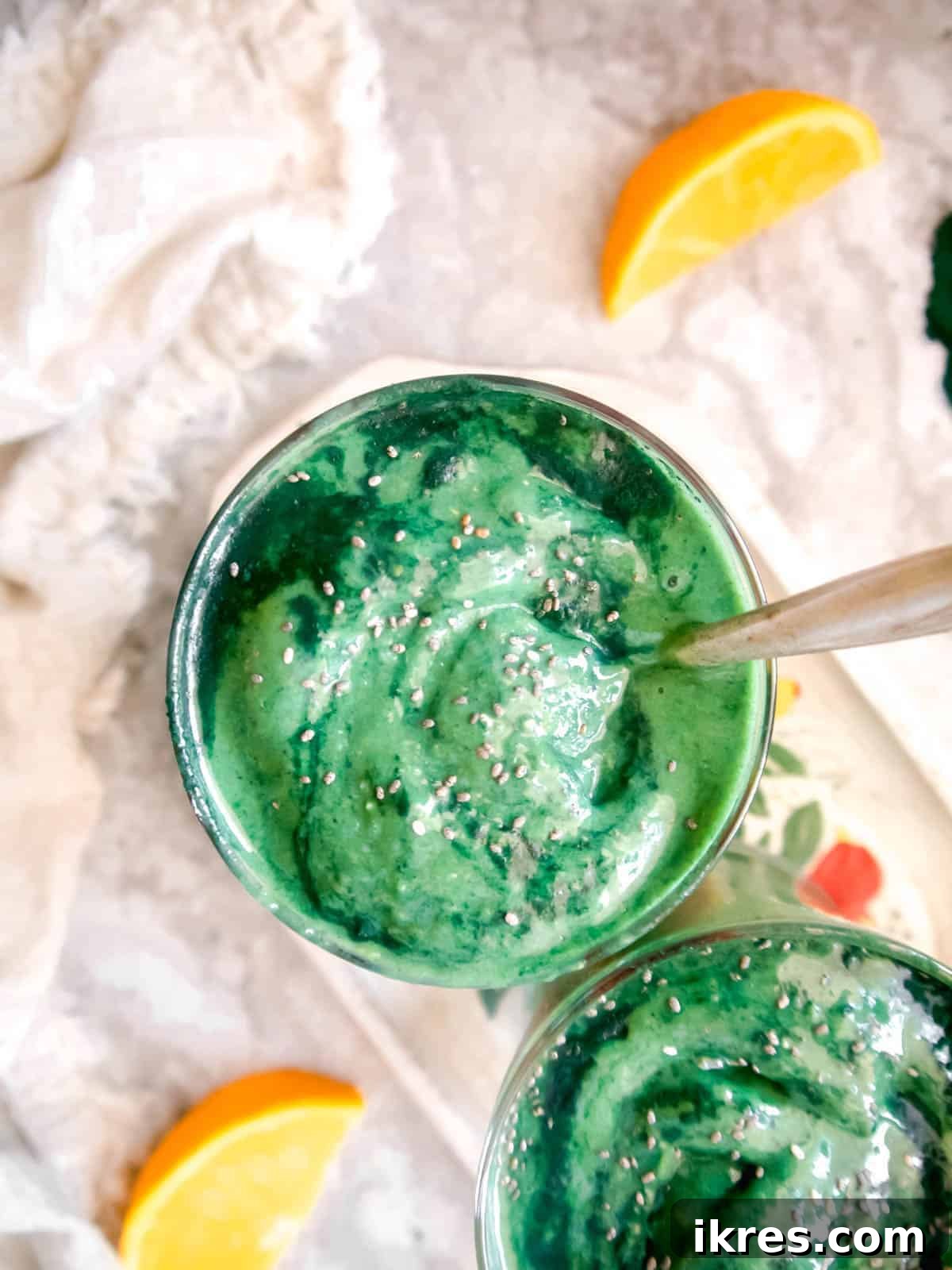Sunrise Spirulina Fusion 5 An overhead shot of a vibrant green spirulina smoothie in a glass, with a spoon resting in it, suggesting a thick, creamy texture, and hints of tropical fruit in the background.