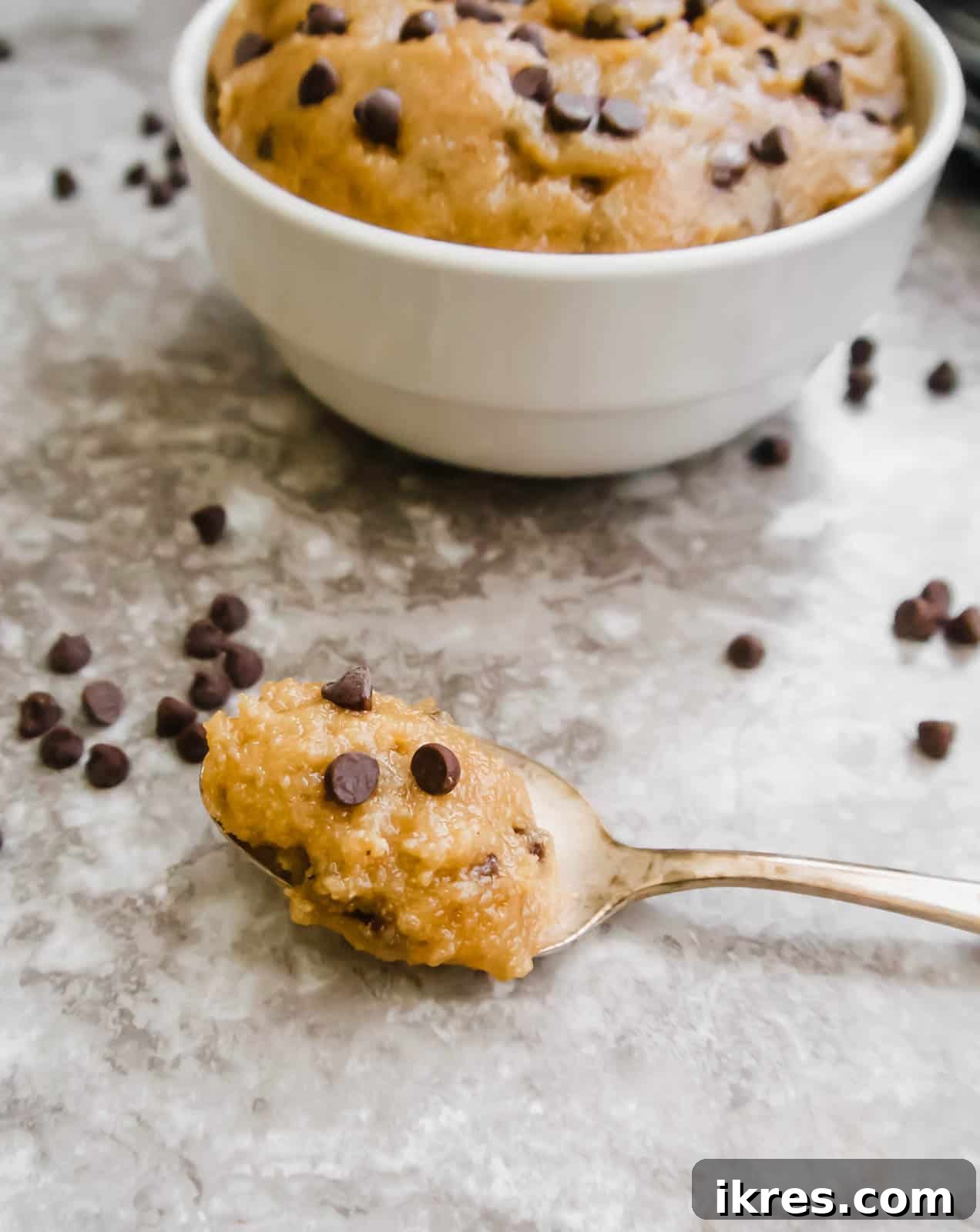 Guilt-Free Gluten-Free Vegan Paleo Cookie Dough 4 A glistening spoon scooping a generous portion of rich, creamy edible chocolate chip cookie dough, vividly showcasing its decadent texture and abundant chocolate flecks, promising a delightful treat.