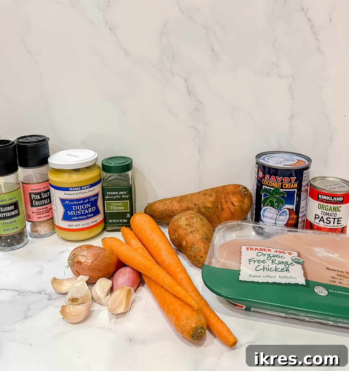 Zesty Dairy-Free Chicken Bake 4 A flat lay of fresh ingredients laid out on a table for making dairy-free chicken casserole with tomato mustard cream sauce, including garlic, onion, carrots, sweet potatoes, chicken, tomato paste, Dijon mustard, coconut cream, and thyme.