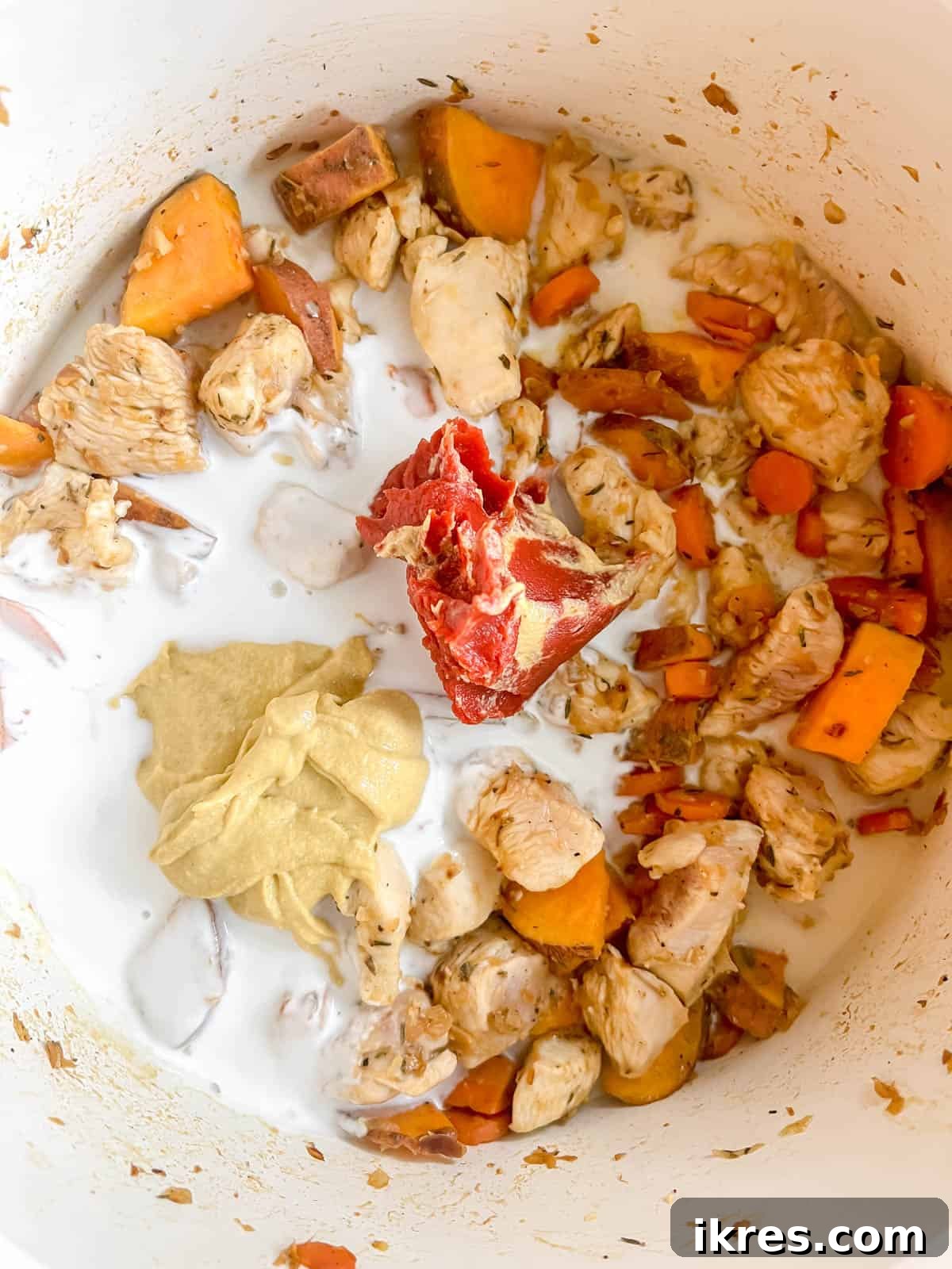 Zesty Dairy-Free Chicken Bake 8 Coconut cream, Dijon mustard, and tomato paste being stirred into the pan with chicken and vegetables to form a creamy sauce.