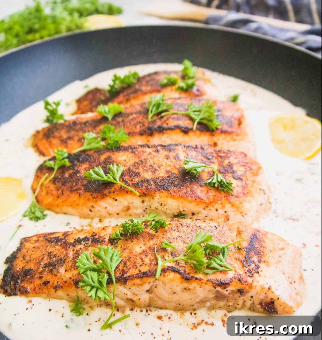 Golden-brown pan-seared salmon simmering in a rich coconut cream sauce within a frying pan.