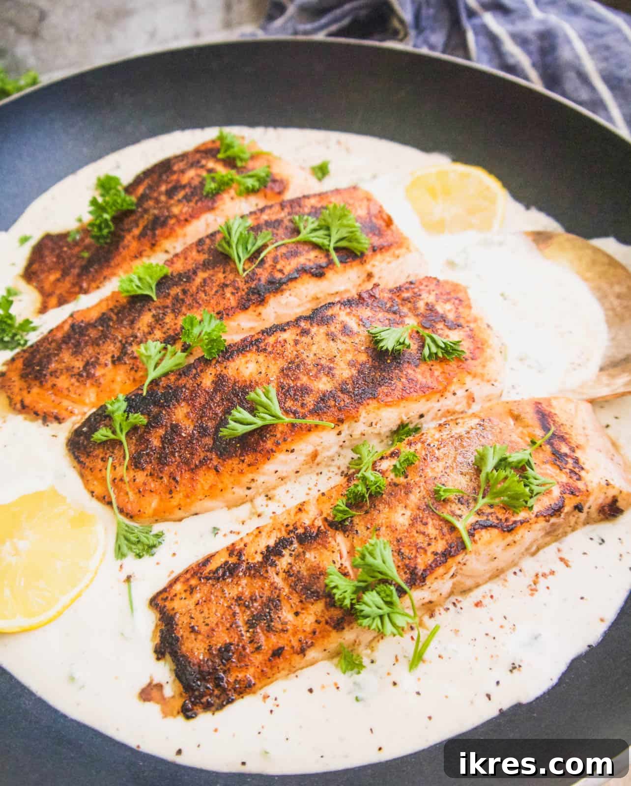 A perfectly cooked salmon fillet soaking in rich coconut cream sauce in a frying pan.