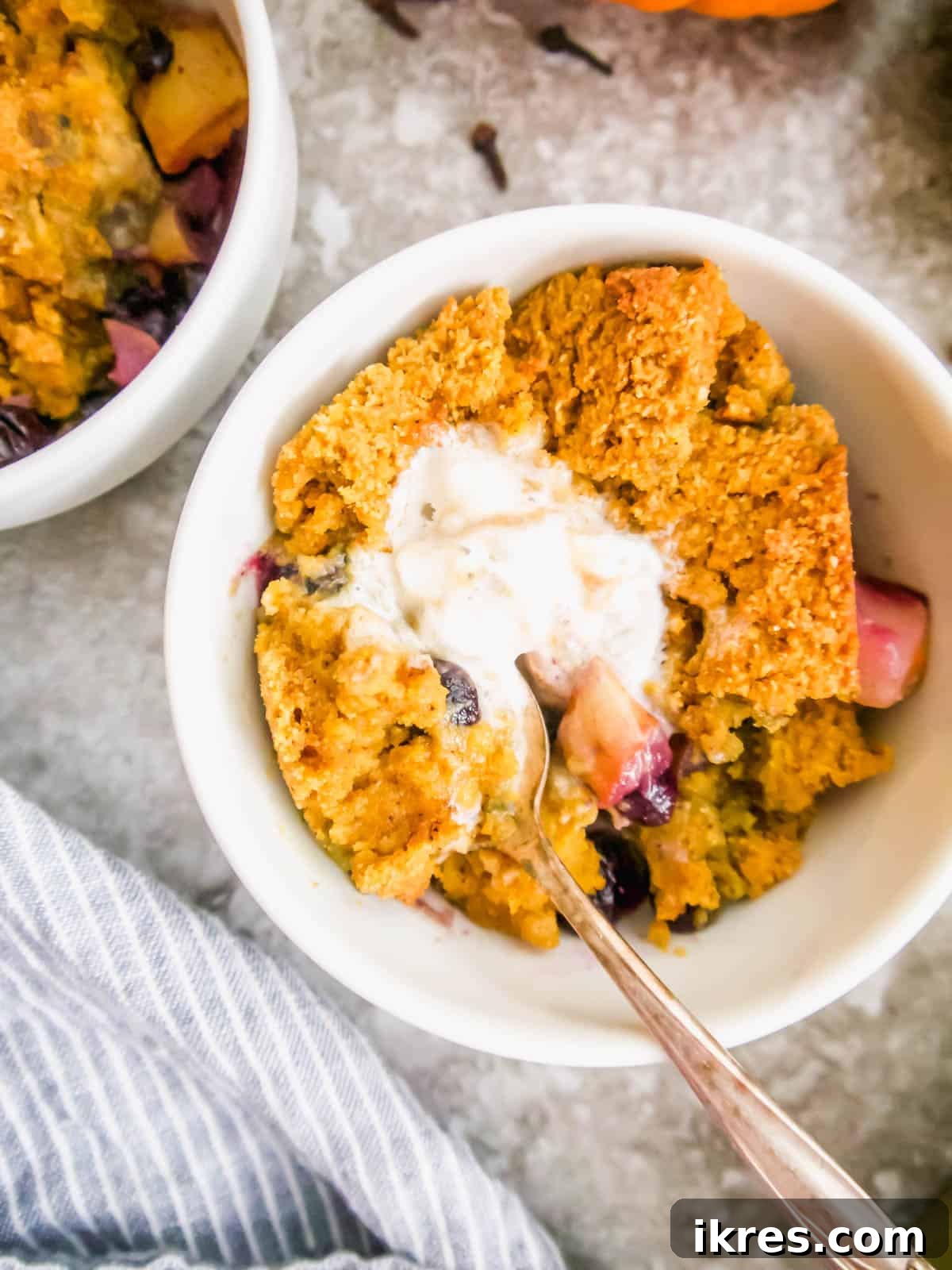 A serving of Gluten-free blueberry and pear cobbler with a scoop of vanilla ice cream on top, ready to be enjoyed.