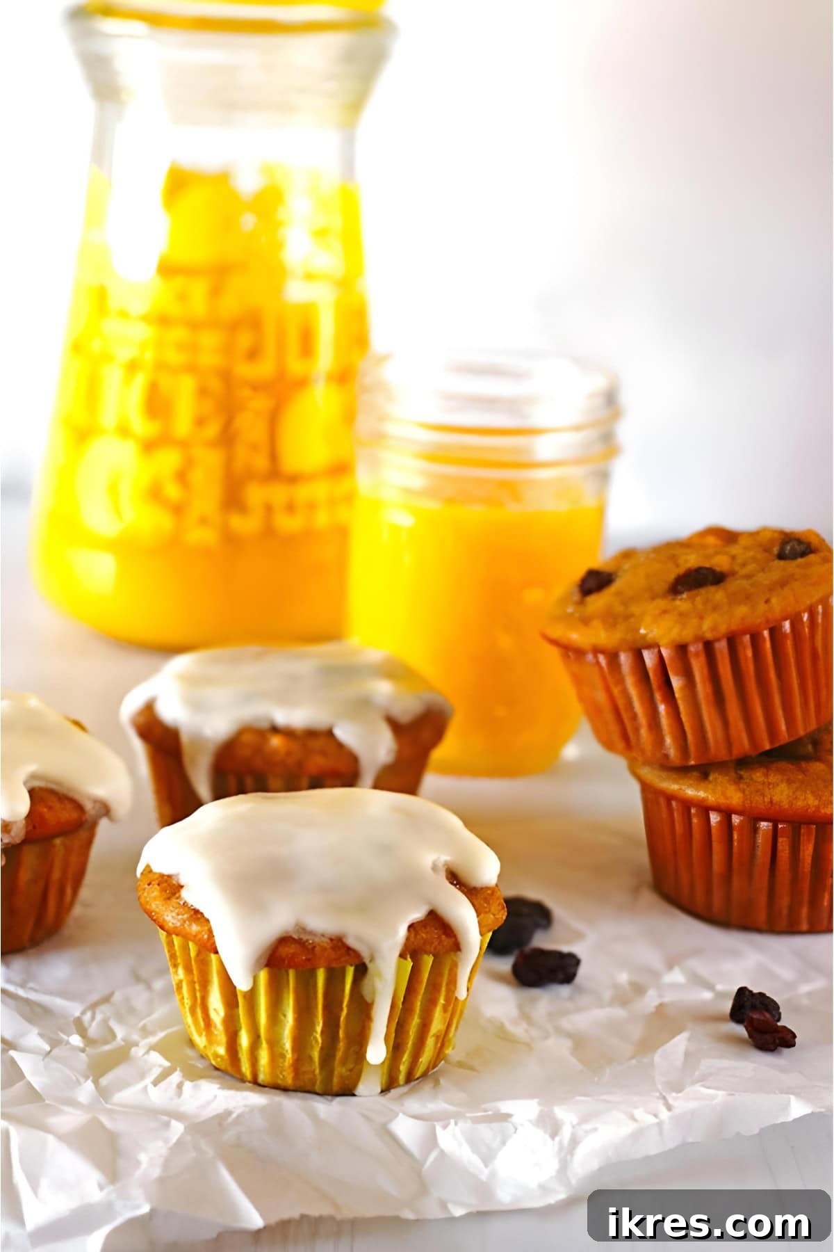 Perfectly Spiced Carrot Cake Muffins with Cream Cheese Glaze 2 Glazed carrot cake muffins on a table with a jug of orange juice.
